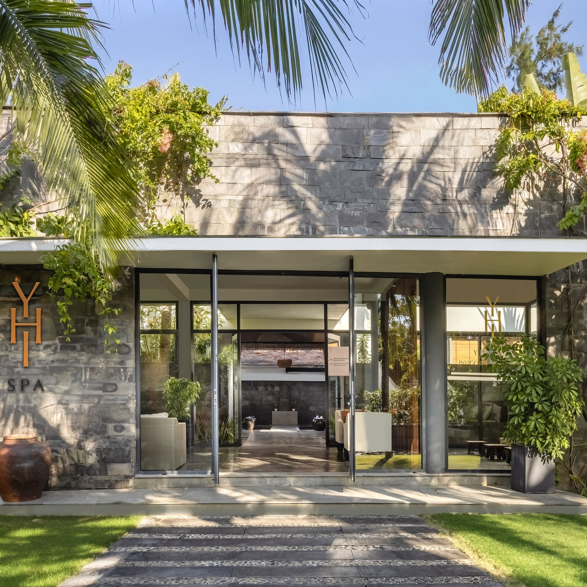 a building with a stone wall and a stone walkway with plants and a stone walkway