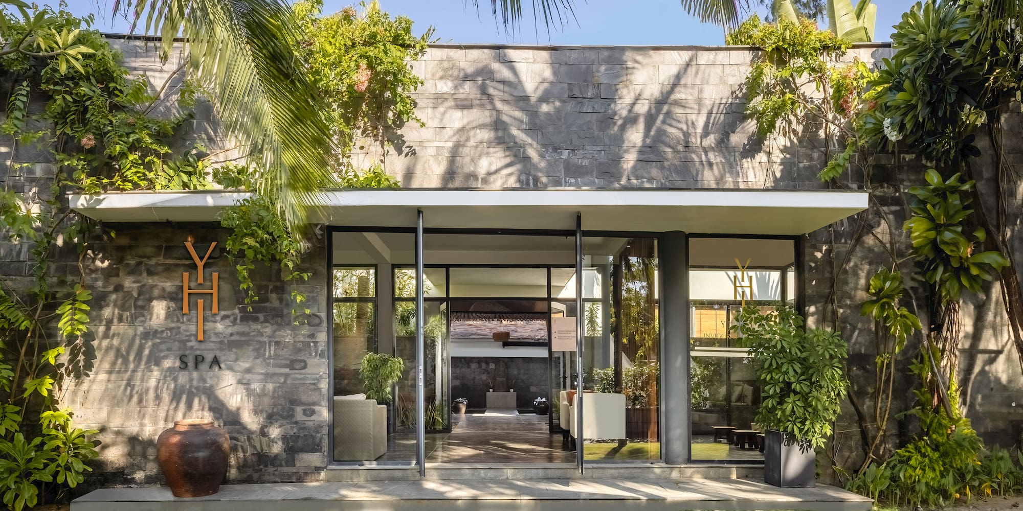 a building with a stone wall and a stone walkway with plants and a stone walkway