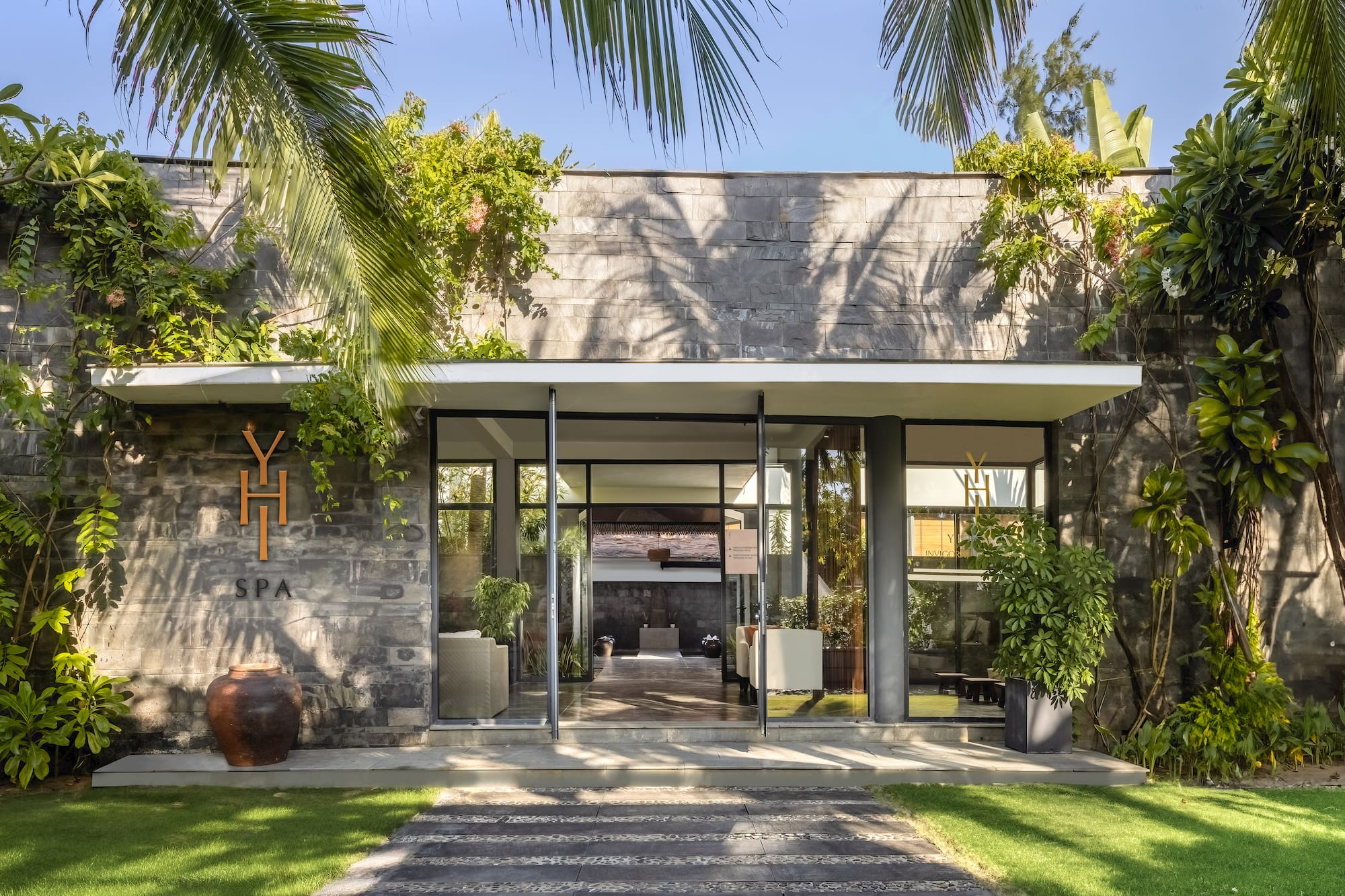 a building with a stone wall and a stone walkway with plants and a stone walkway