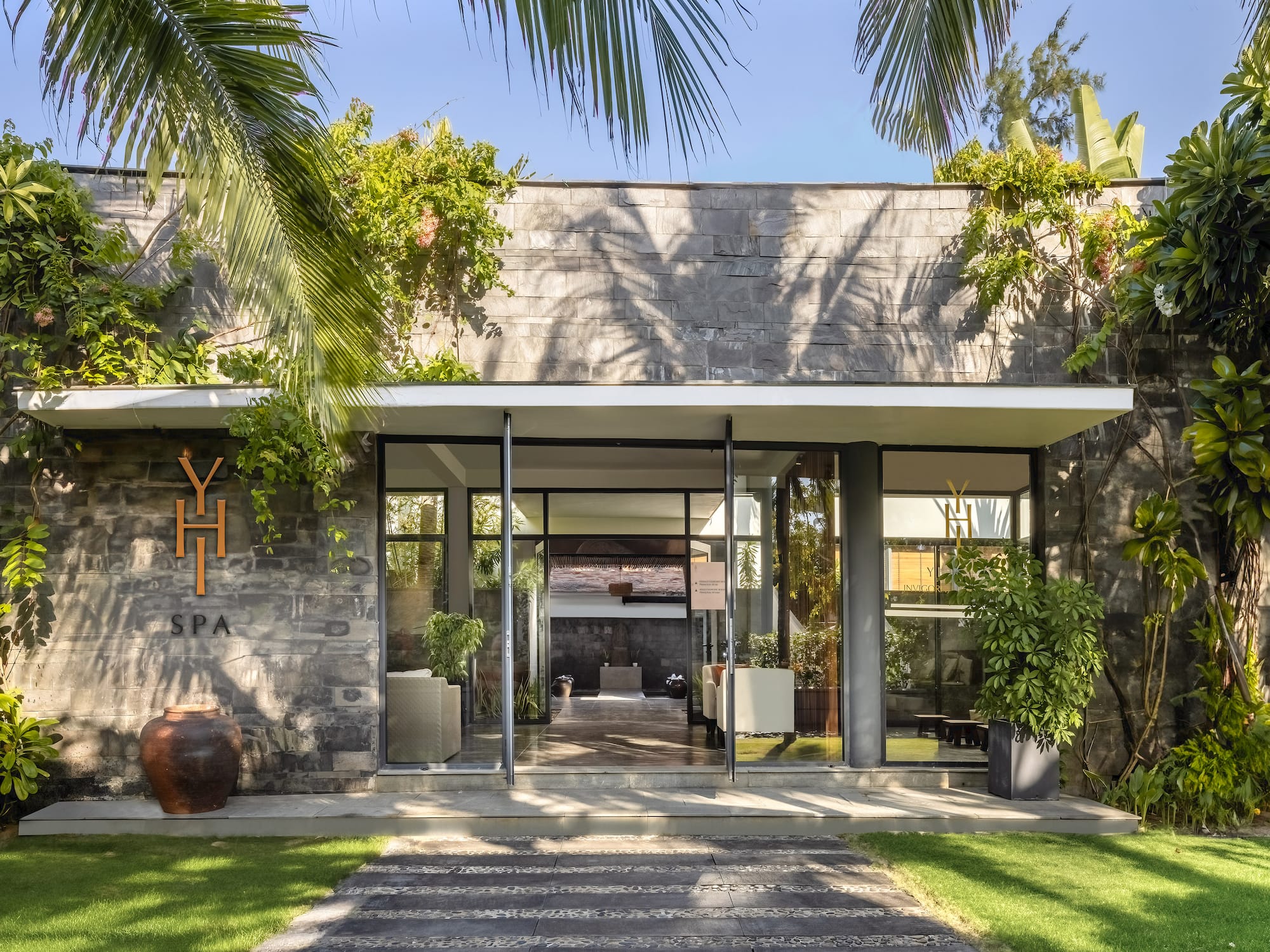 a building with a stone wall and a stone walkway with plants and a stone walkway