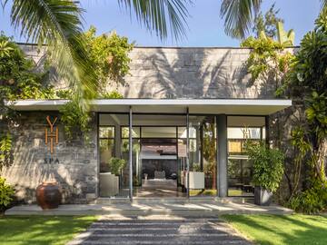 a building with a stone wall and a stone walkway with plants and a stone walkway