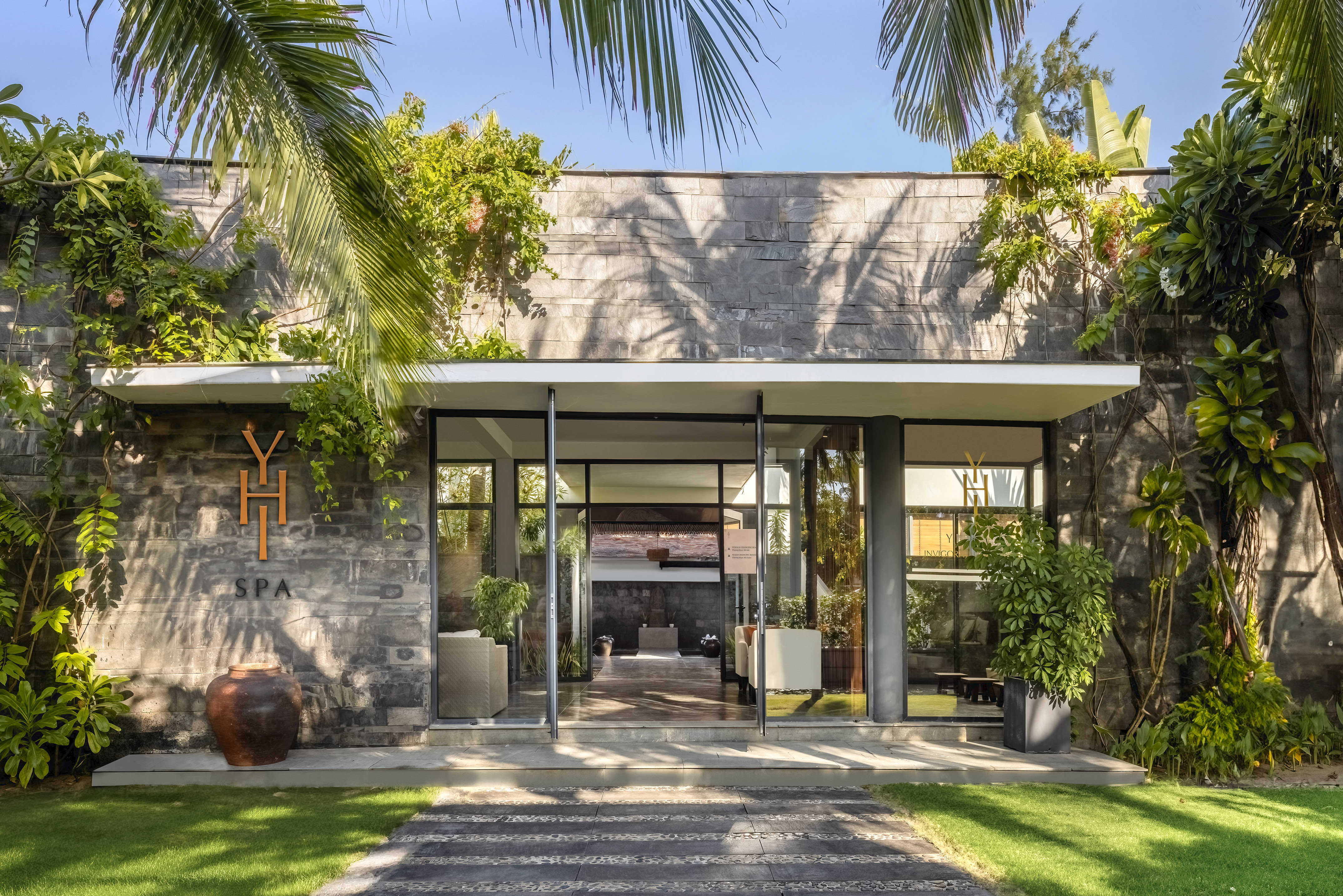 a building with a stone wall and a stone walkway with plants and a stone walkway