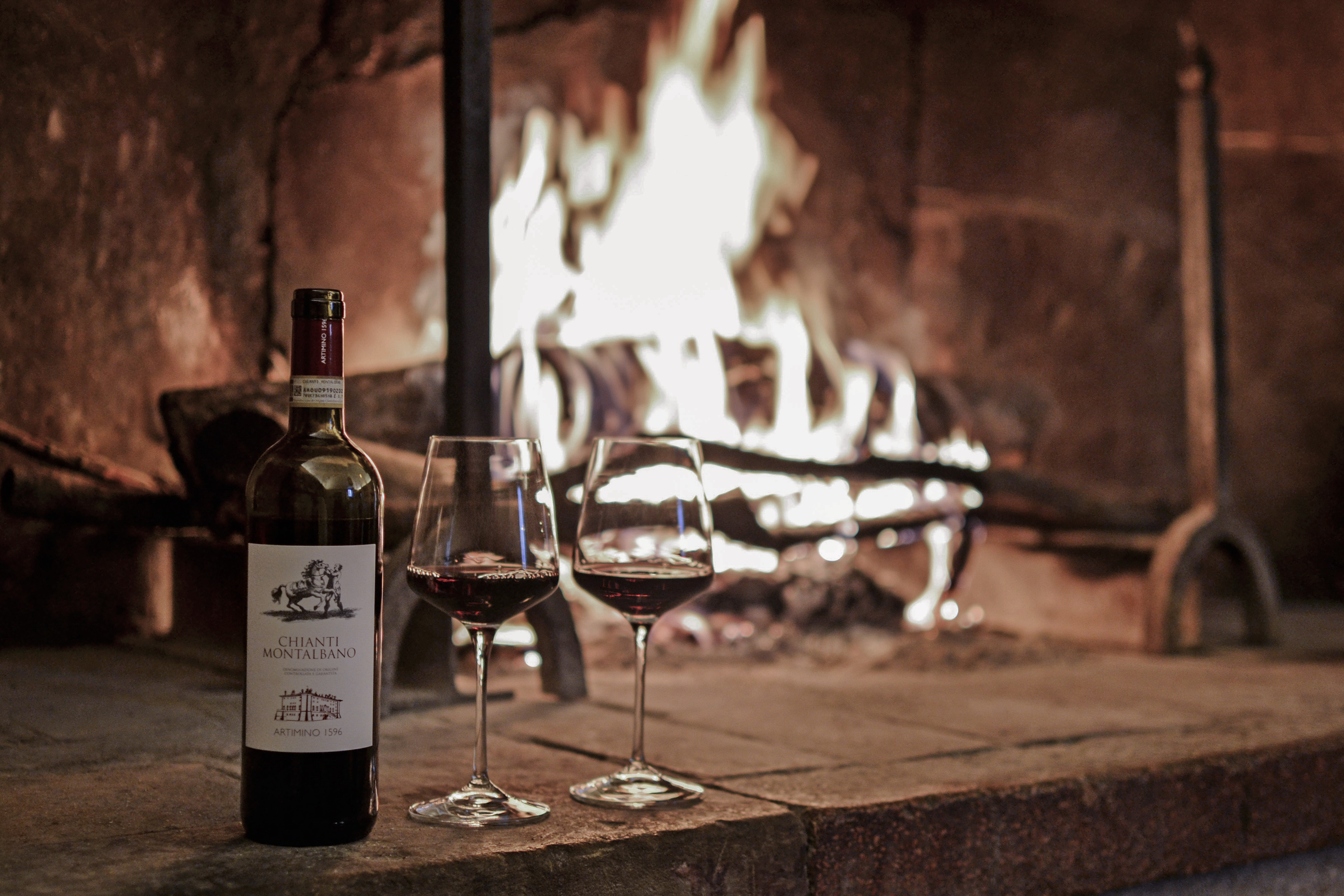 a bottle of wine and two glasses of wine in front of a fireplace