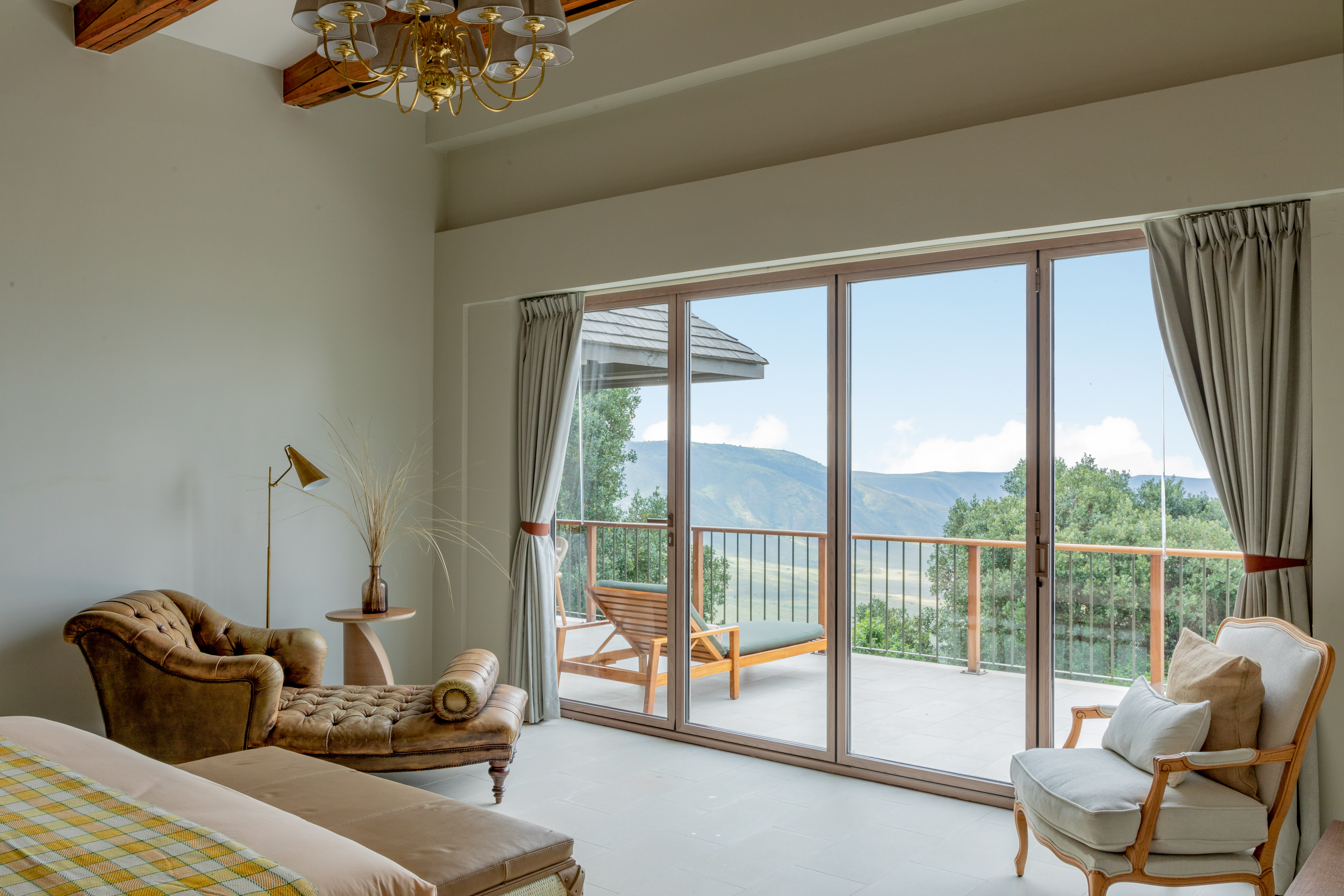 Luxury bedroom with mountain view balcony, chaise lounge, and green landscape.