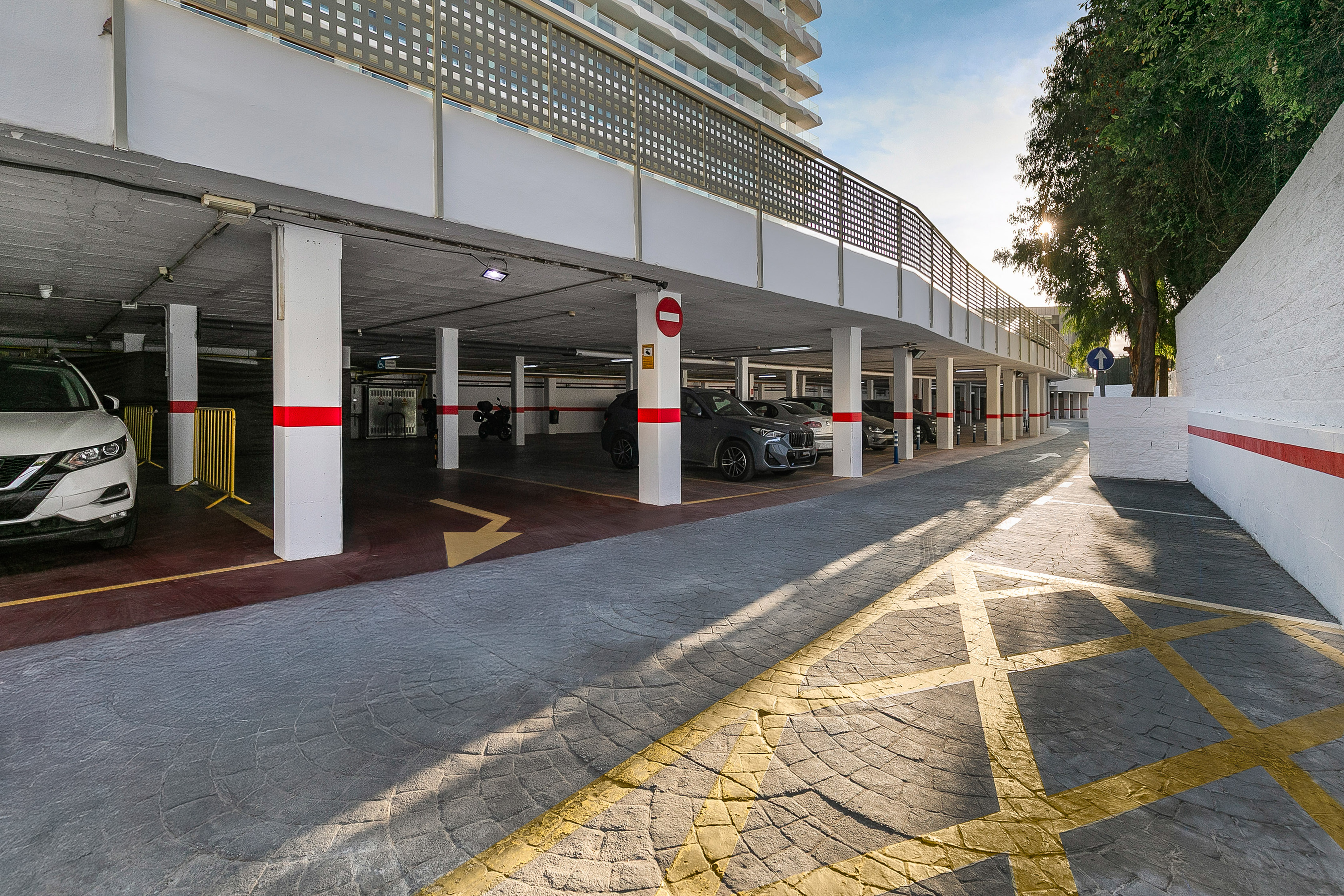 Sunny underground parking garage with cars, red-striped pillars, and yellow markings.