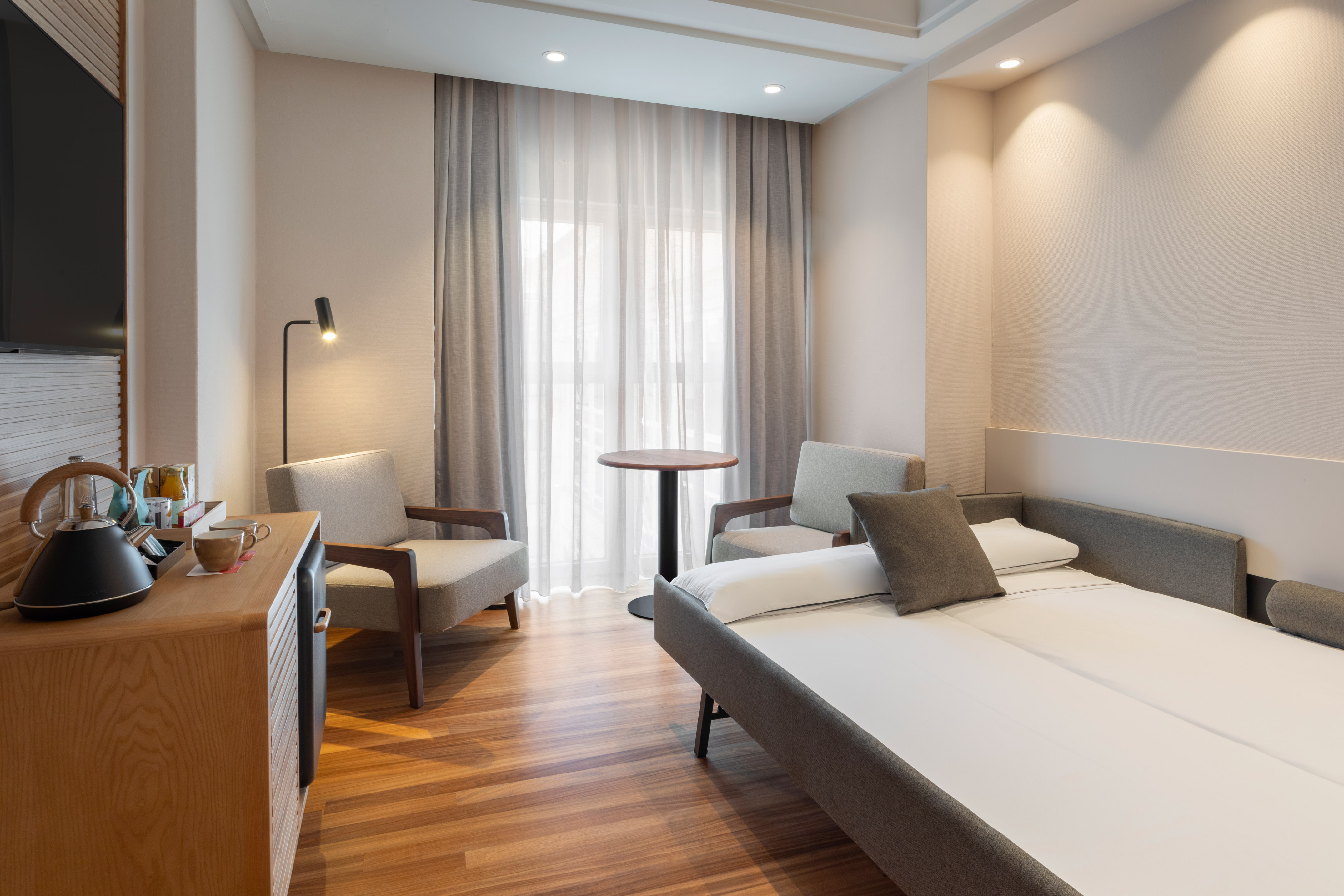 Modern hotel room with sofa bed, two armchairs, and wooden furnishings.