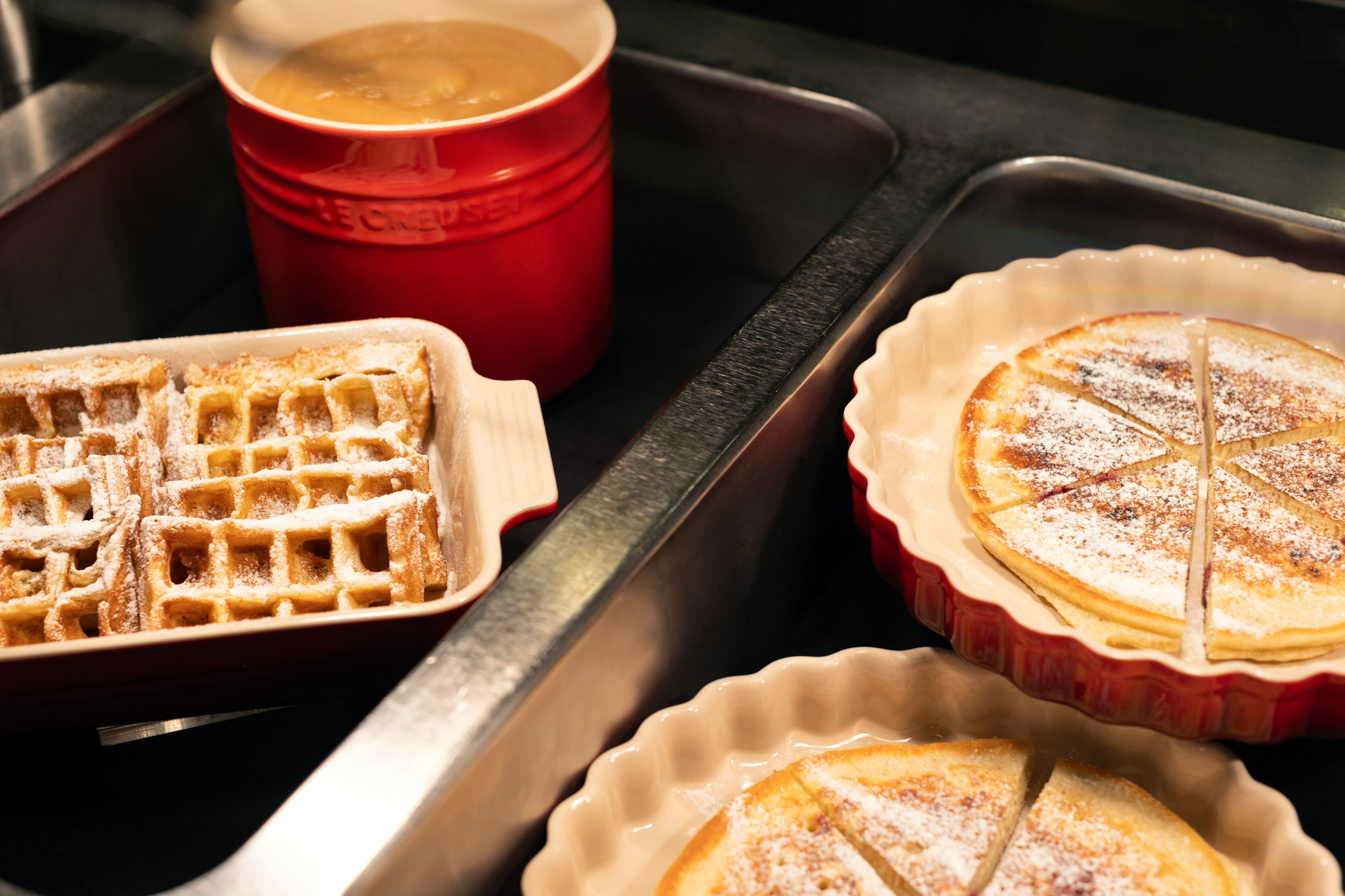 Powdered sugar waffles, sliced pancakes, and sauce in Le Creuset pot.