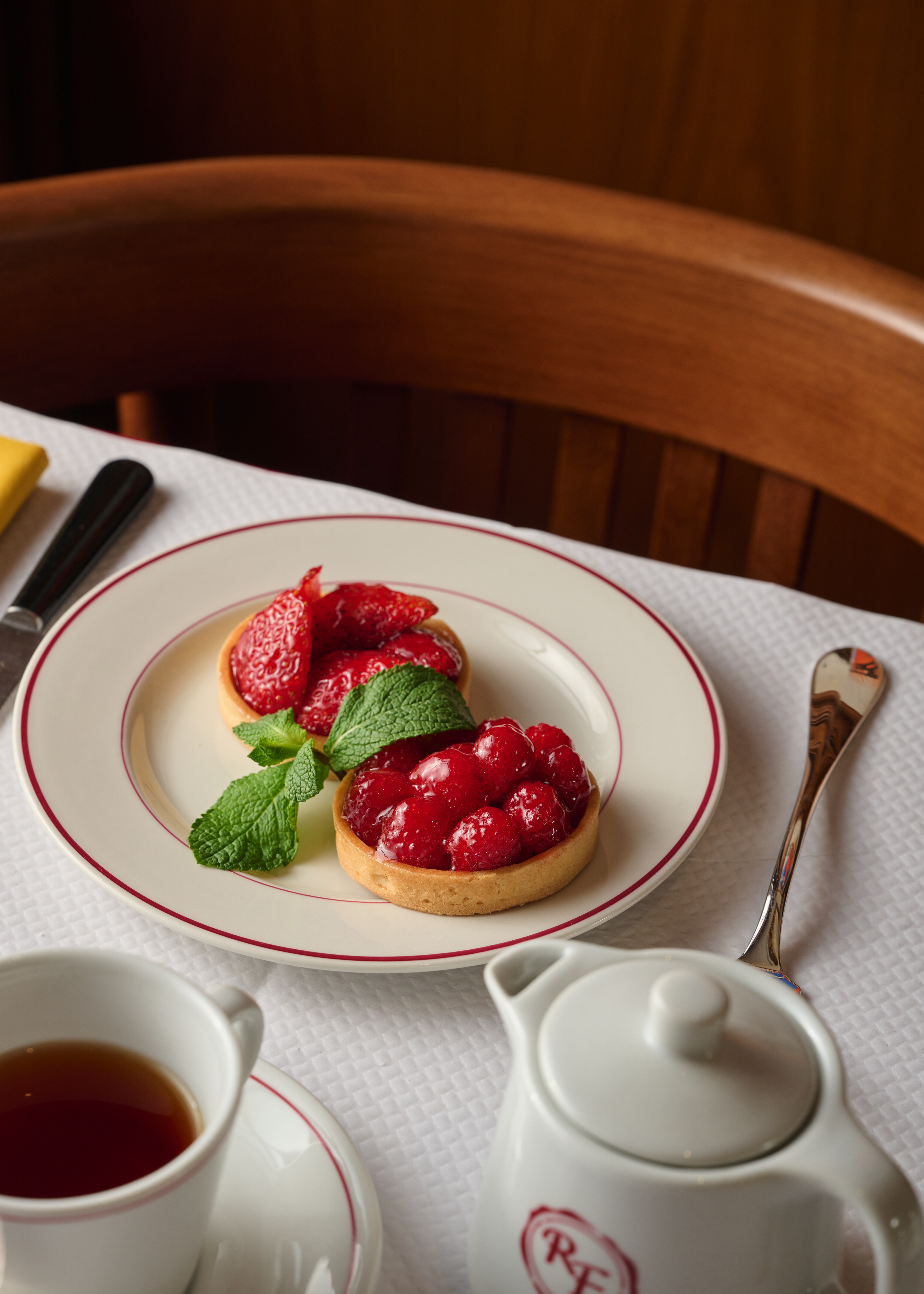 Strawberry and raspberry tarts with mint, tea, and teapot on white tablecloth.