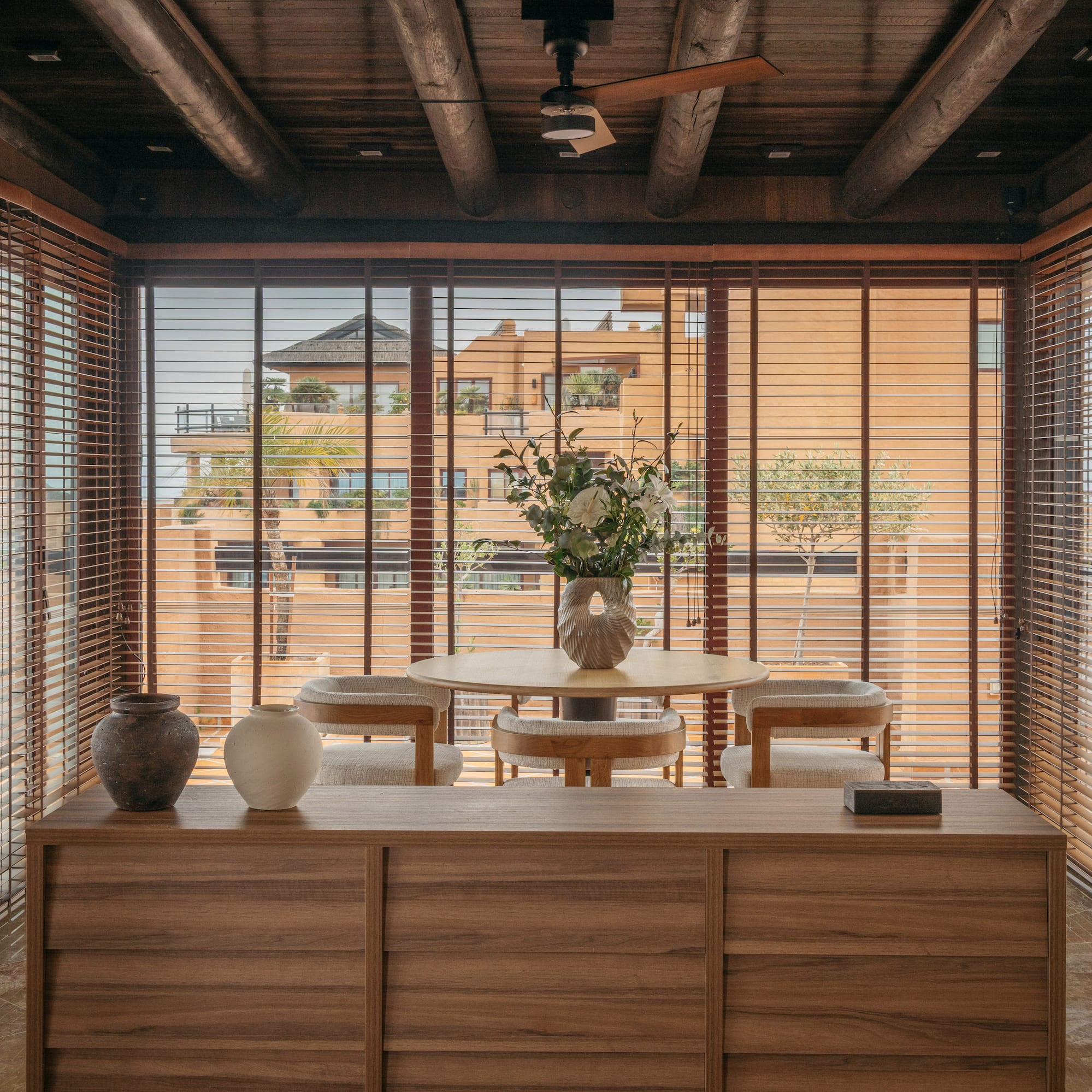 Dining space with wooden blinds, exposed beams, and outside building view.