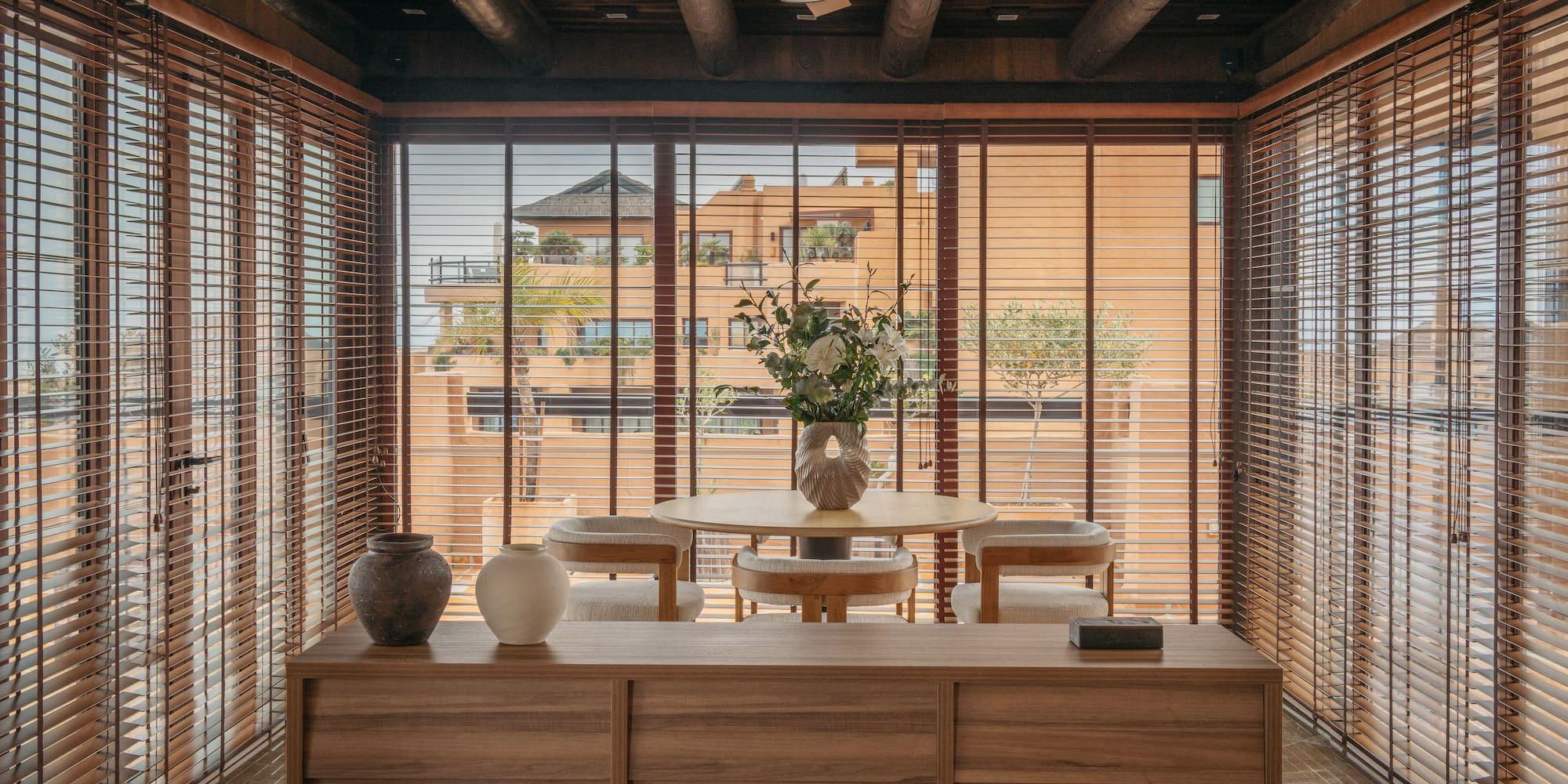 Dining space with wooden blinds, exposed beams, and outside building view.