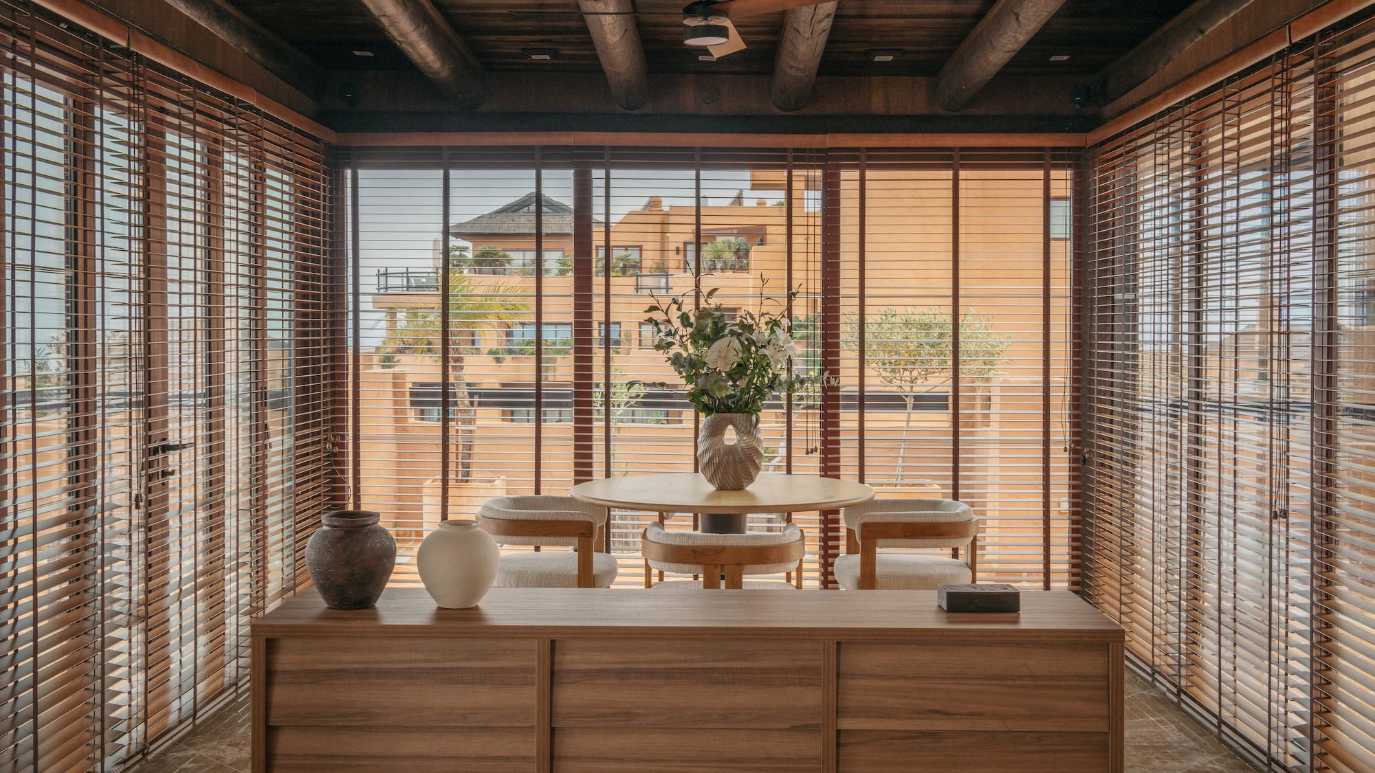 Dining space with wooden blinds, exposed beams, and outside building view.