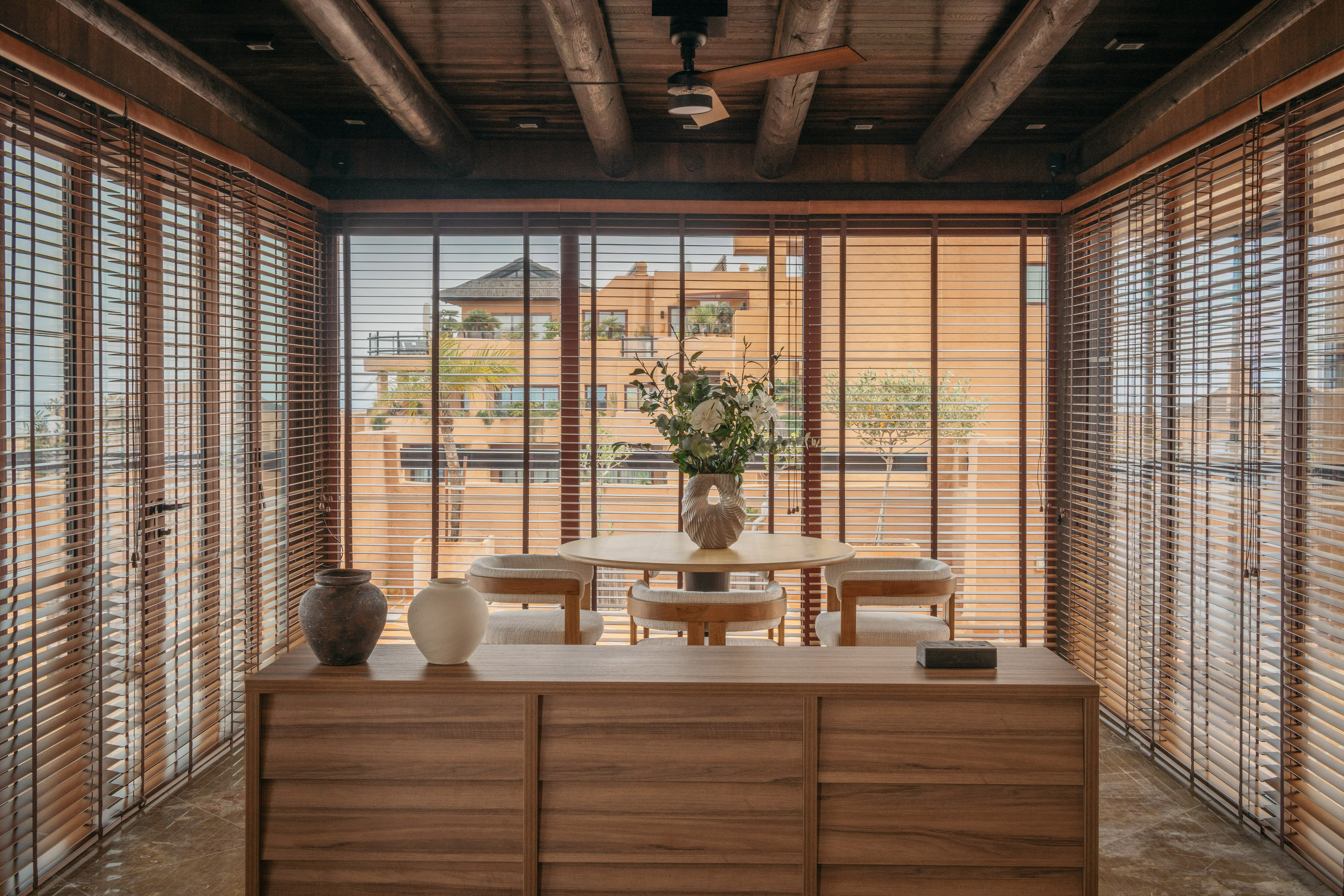 Dining space with wooden blinds, exposed beams, and outside building view.