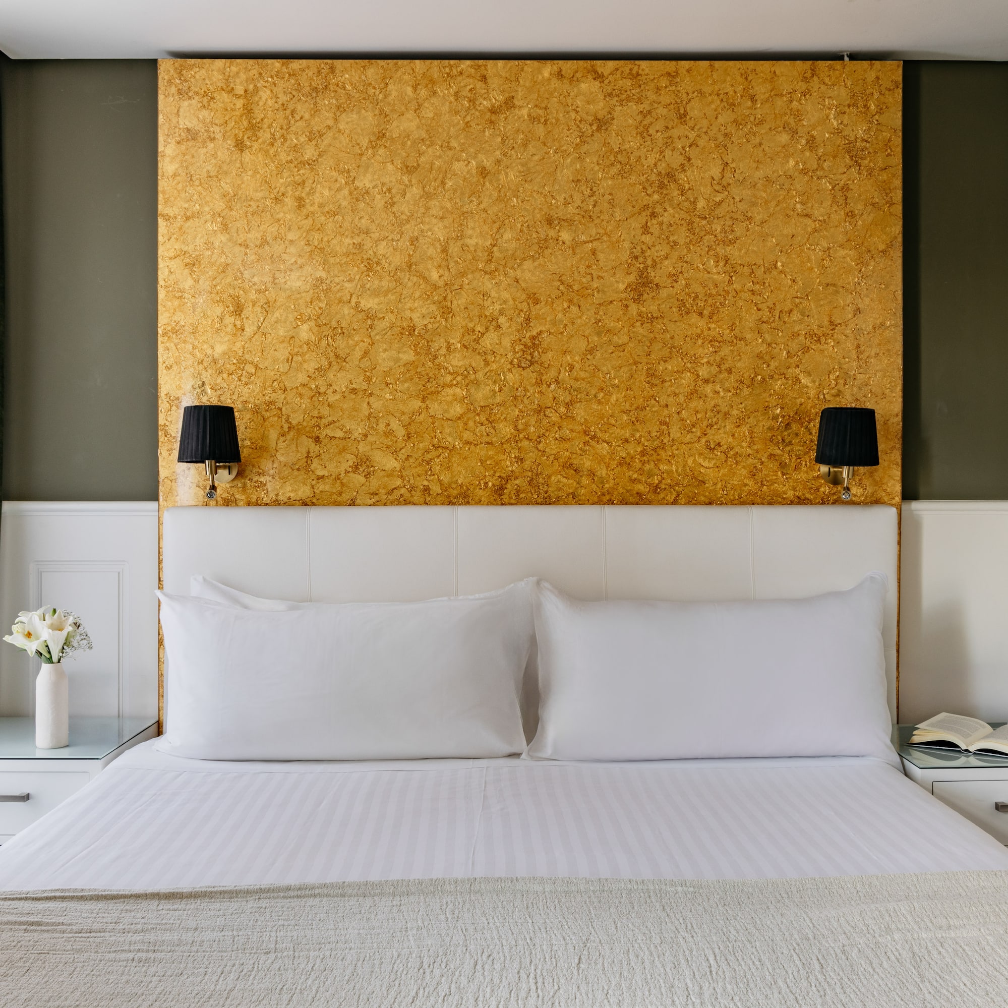 Dormitorio hotel: cama doble, cabecero blanco, pared dorada y apliques.