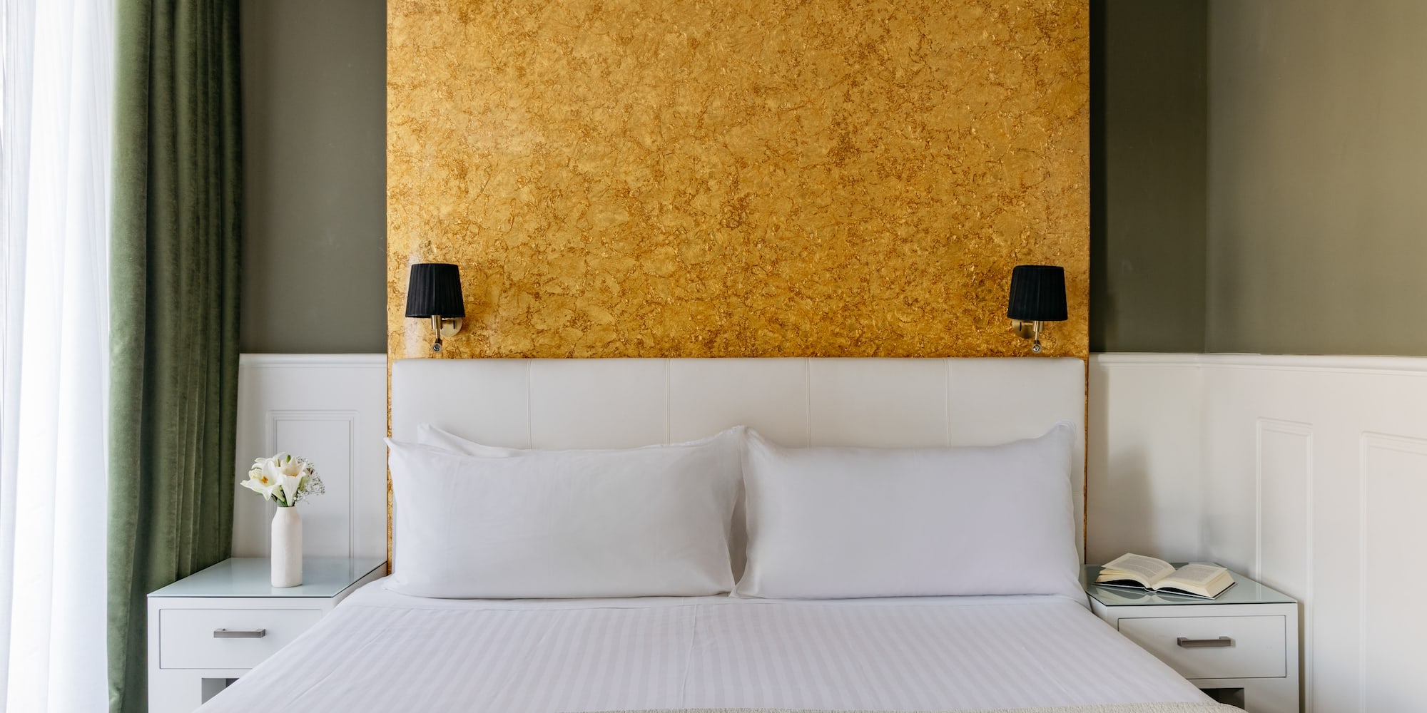 Dormitorio hotel: cama doble, cabecero blanco, pared dorada y apliques.