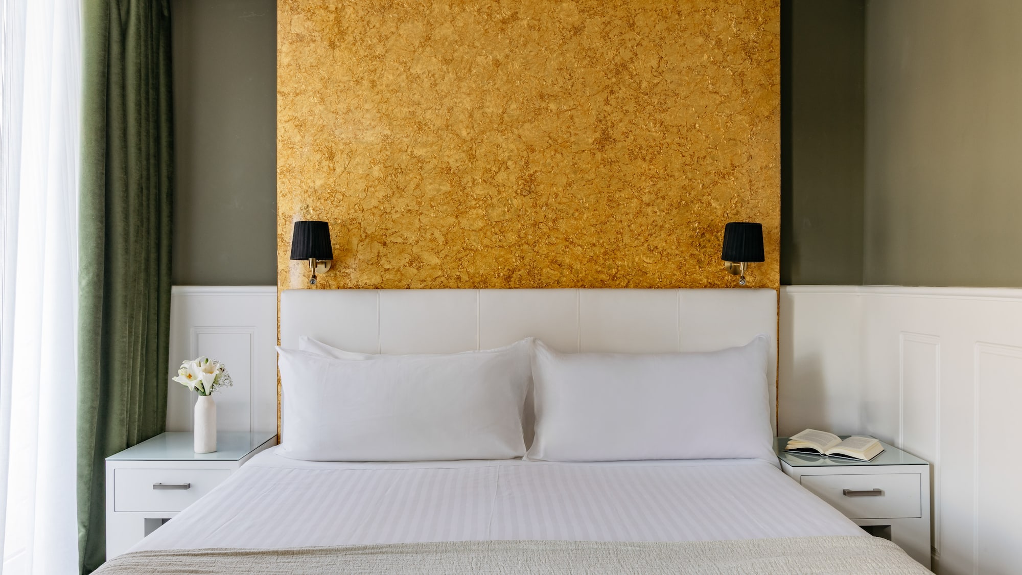 Dormitorio hotel: cama doble, cabecero blanco, pared dorada y apliques.