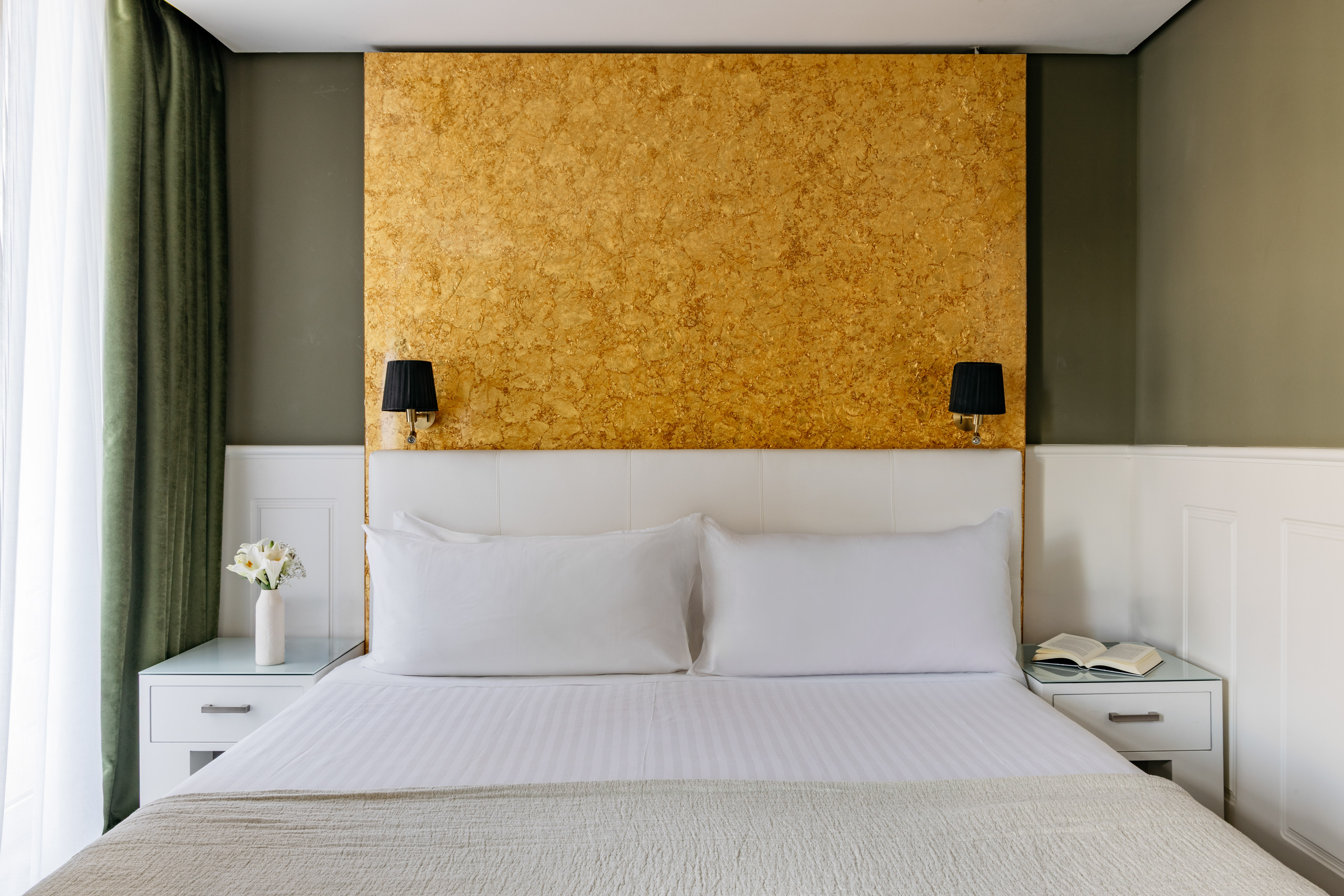 Dormitorio hotel: cama doble, cabecero blanco, pared dorada y apliques.