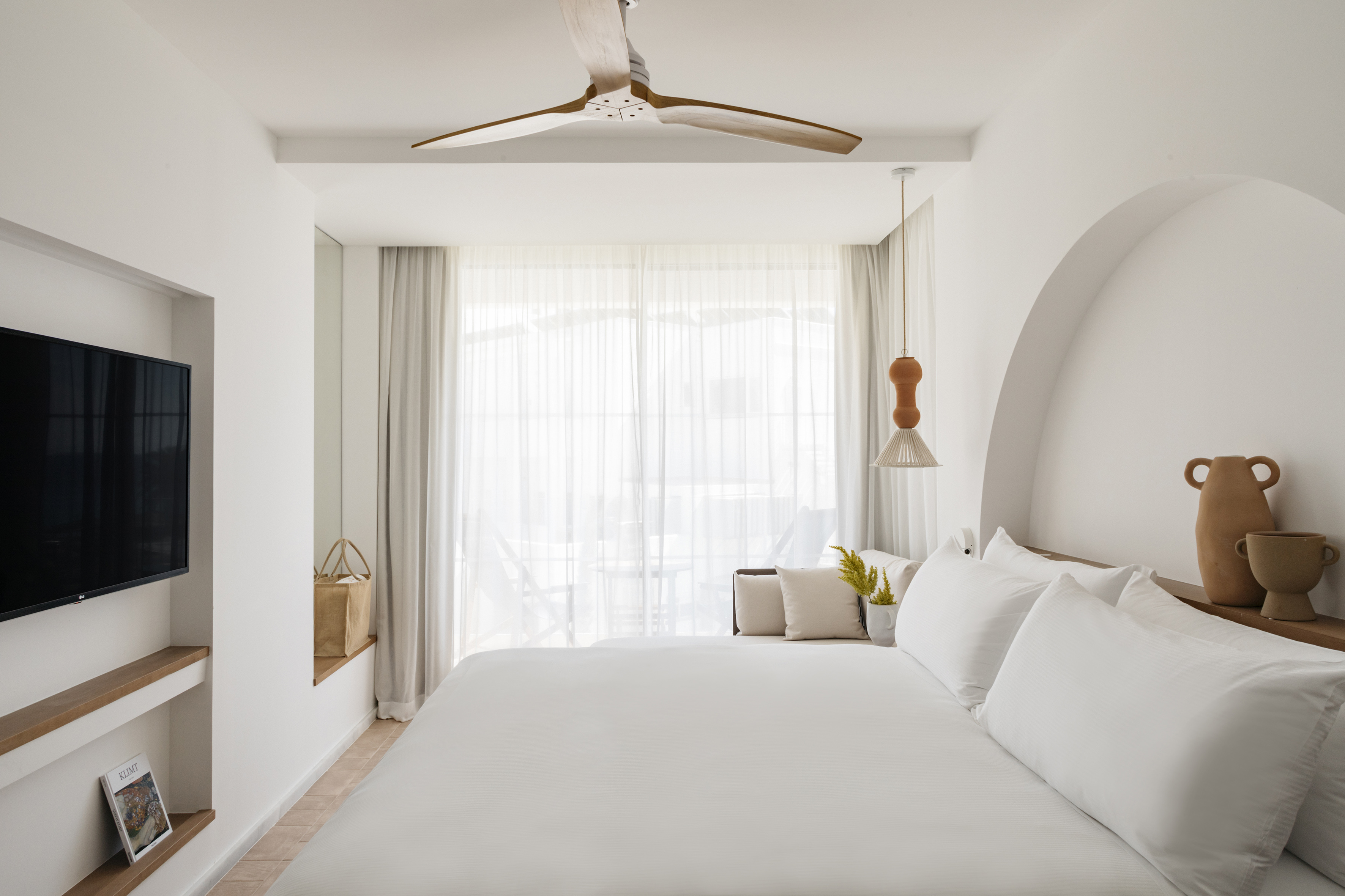 a white bed with white sheets and a ceiling fan