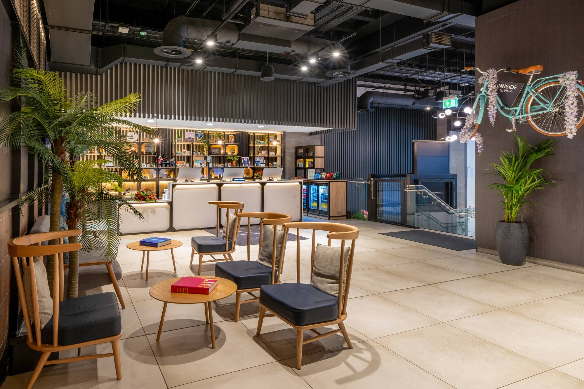 Modern hotel reception lobby with seating, palm trees, and bicycle wall decor.