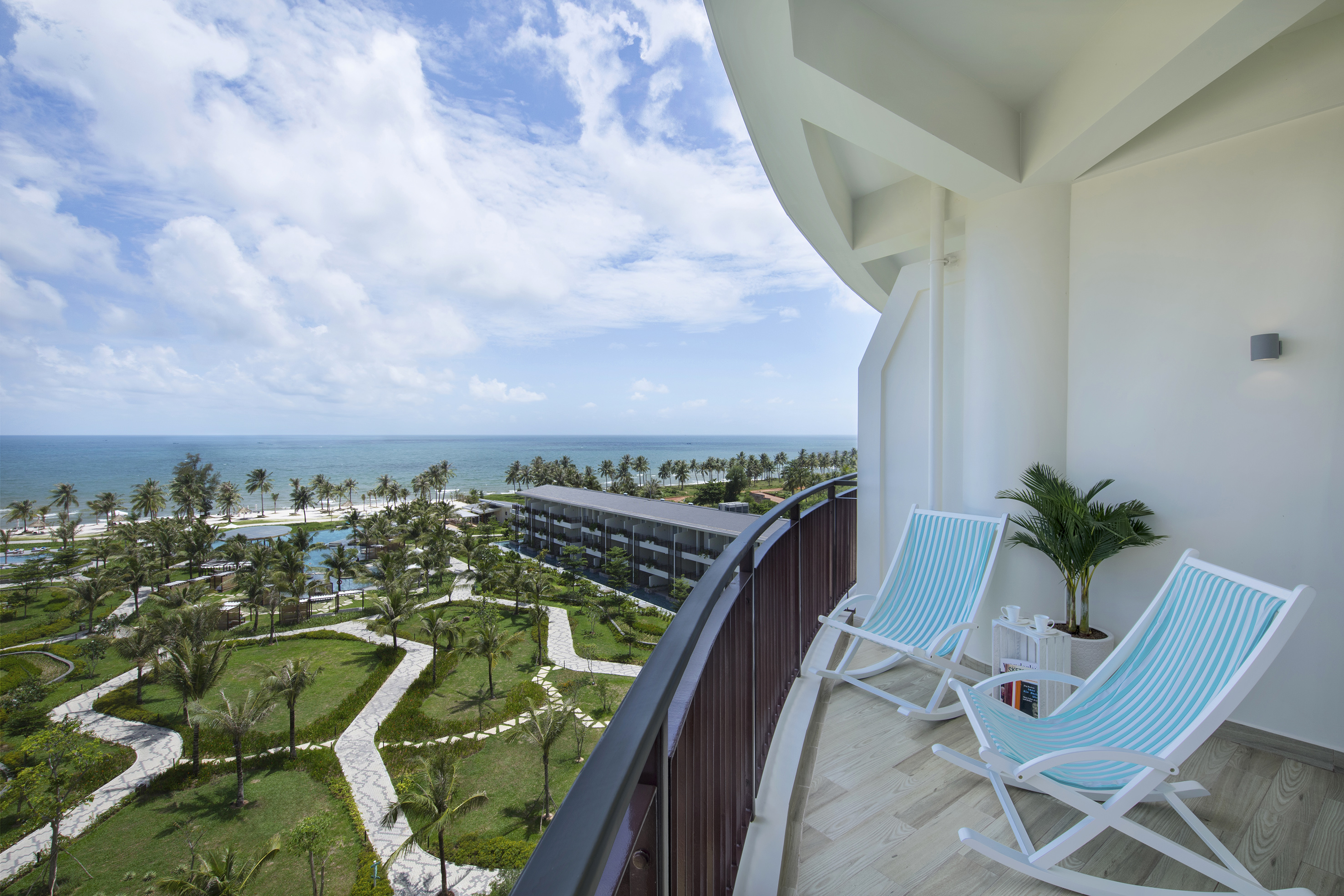 Balcony with ocean view, striped chairs, tropical resort, palm trees, beach.