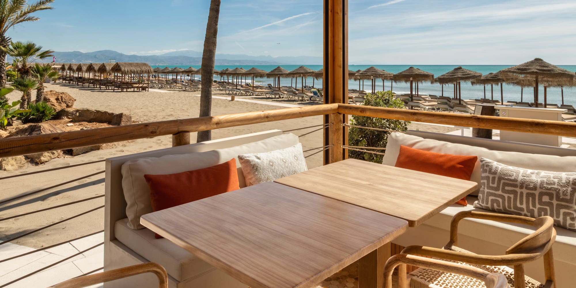 Beachfront dining terrace with sea view, sandy beach, and straw parasols.
