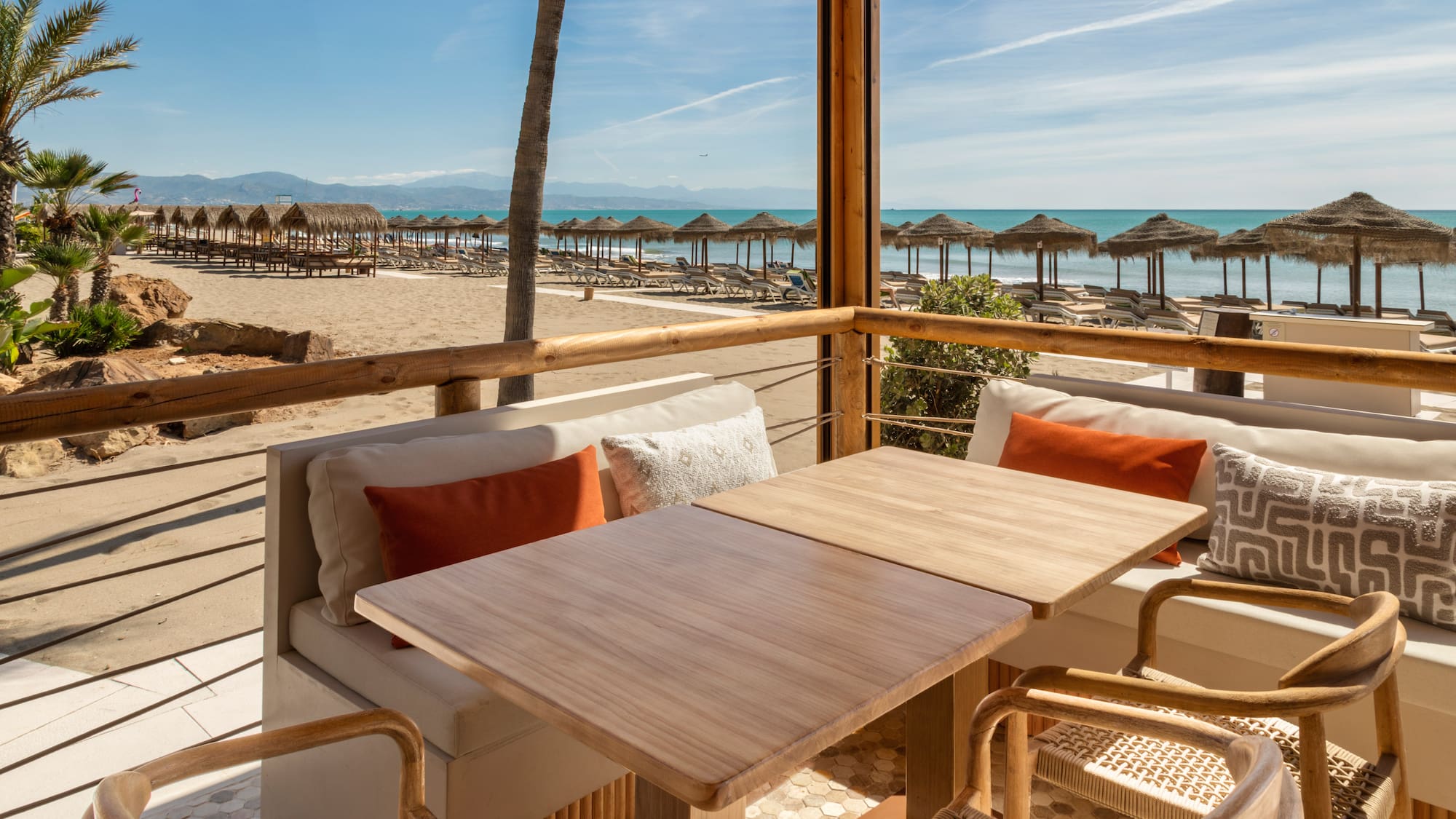 Beachfront dining terrace with sea view, sandy beach, and straw parasols.