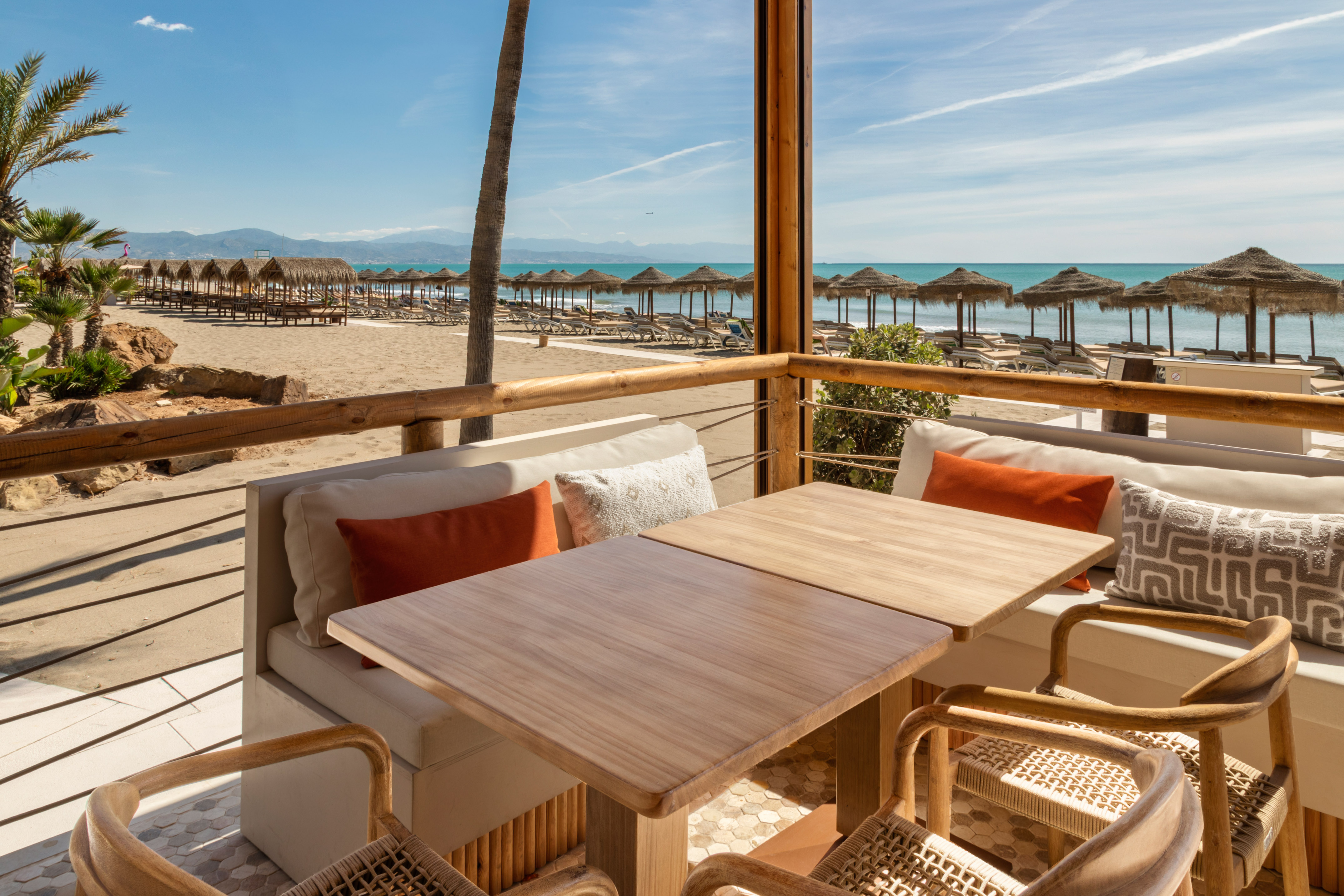 Beachfront dining terrace with sea view, sandy beach, and straw parasols.