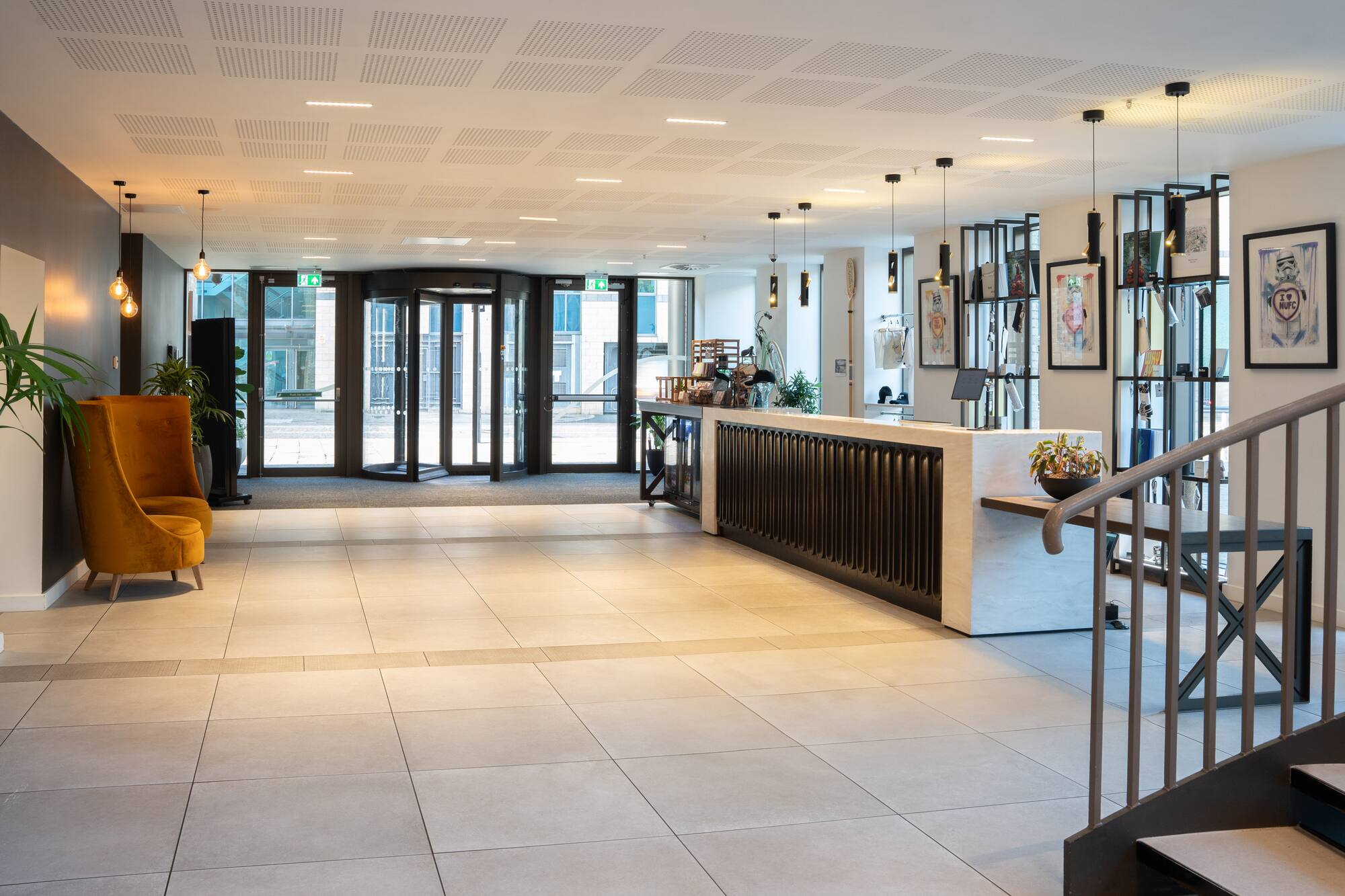 Modern hotel lobby with reception desk, revolving door, and accent chairs.