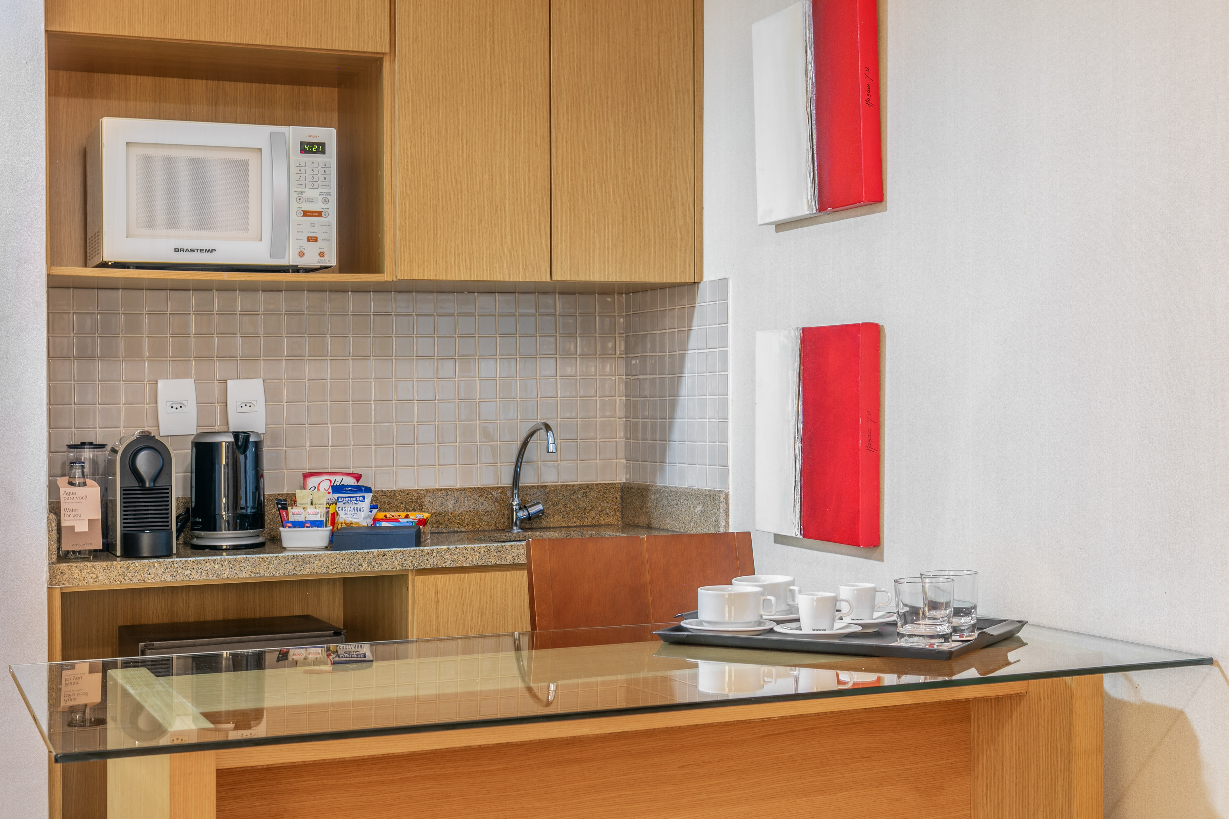 Hotel kitchenette with microwave, coffee machine, sink, and bar area.