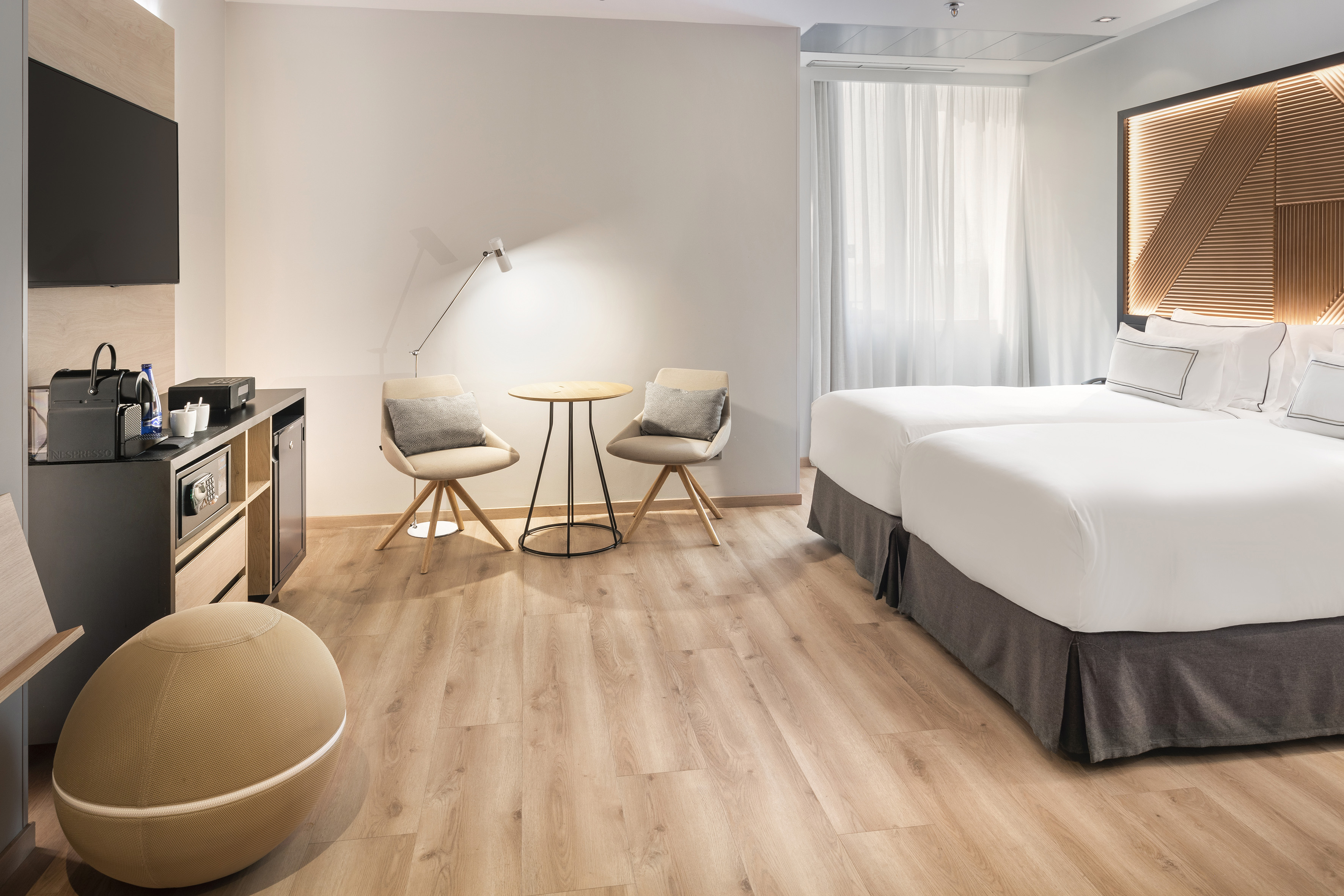 Modern hotel room with twin beds, wooden floor, Nespresso, and seating.