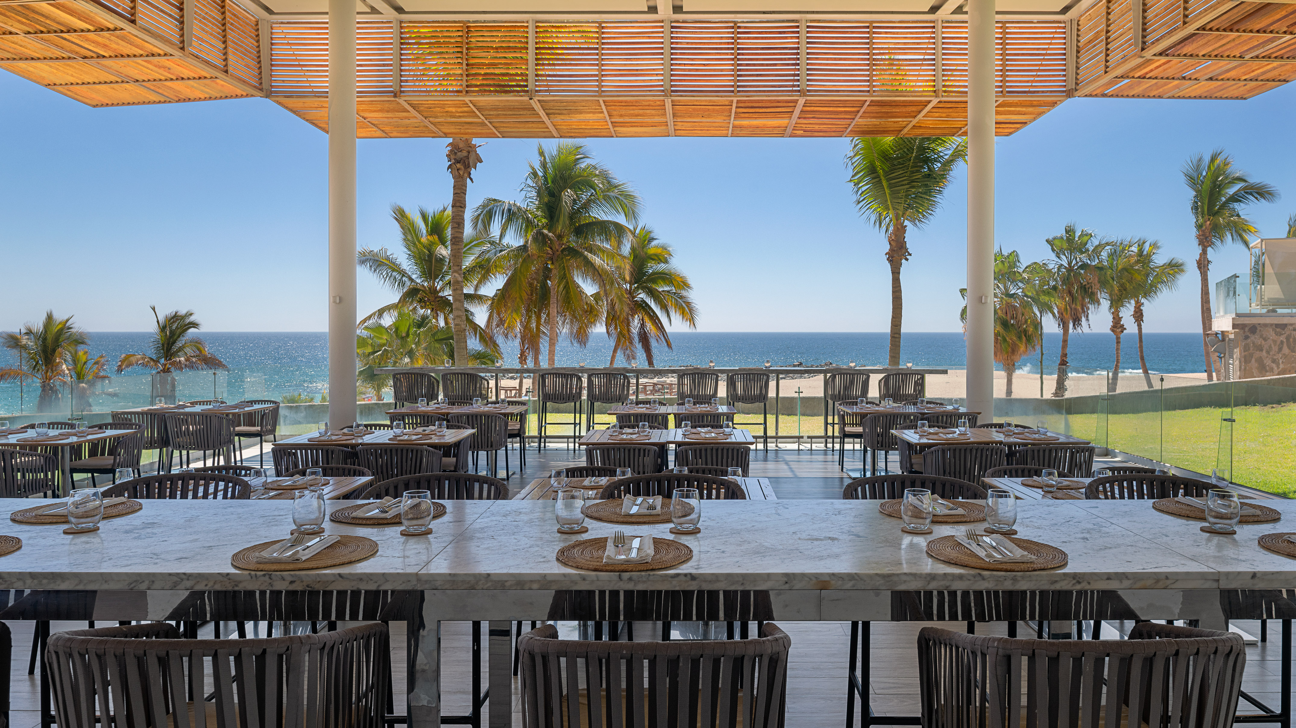 Beachfront restaurant, outdoor dining with ocean view and tropical palm trees.