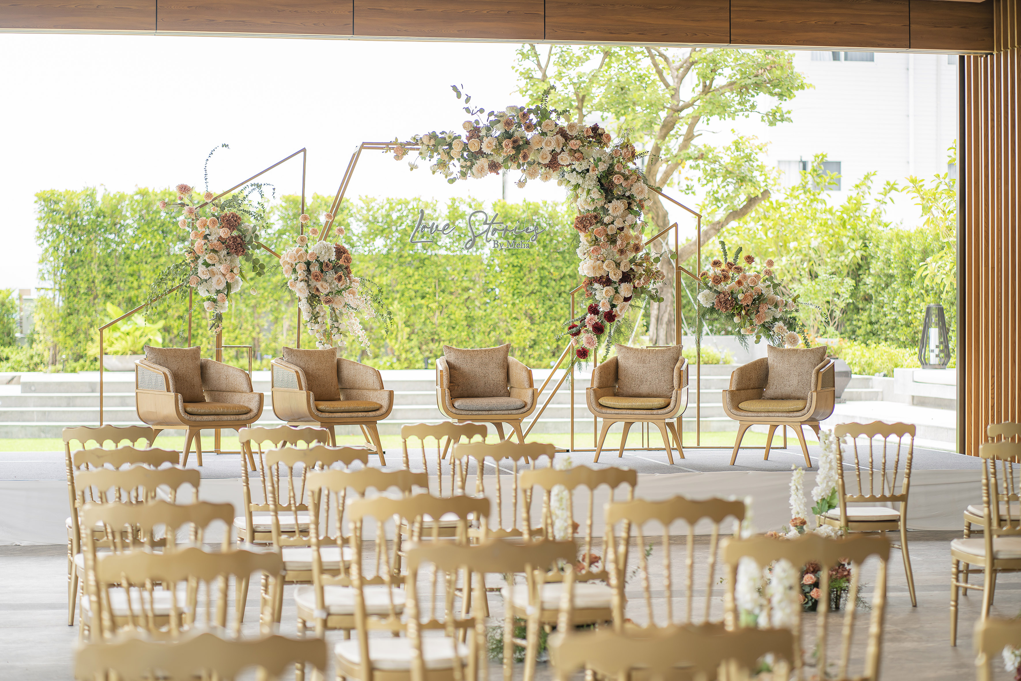 Outdoor wedding ceremony decor with floral geometric arch and gold chairs.