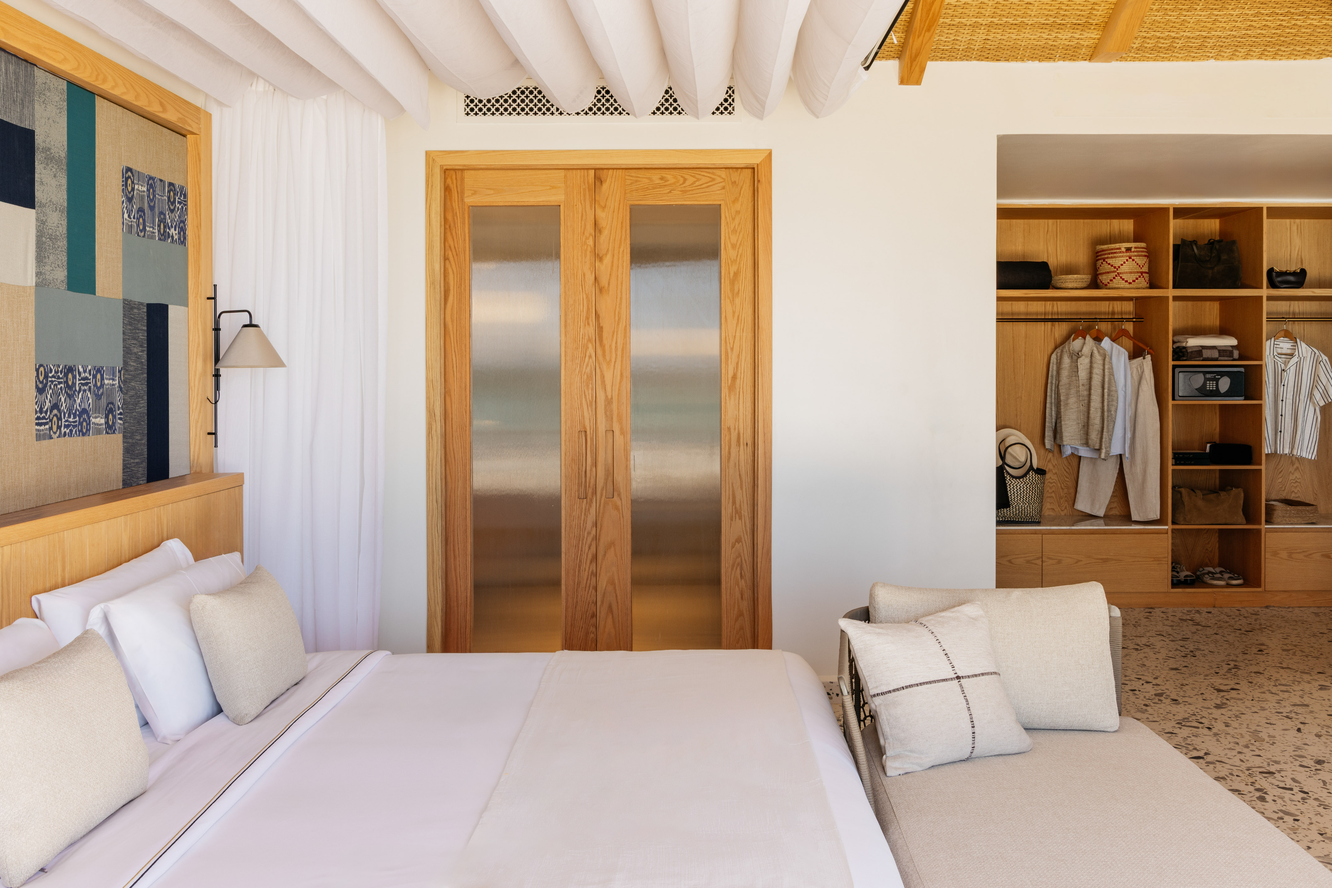 Modern hotel bedroom with white bed, open wooden wardrobe, and daybed.
