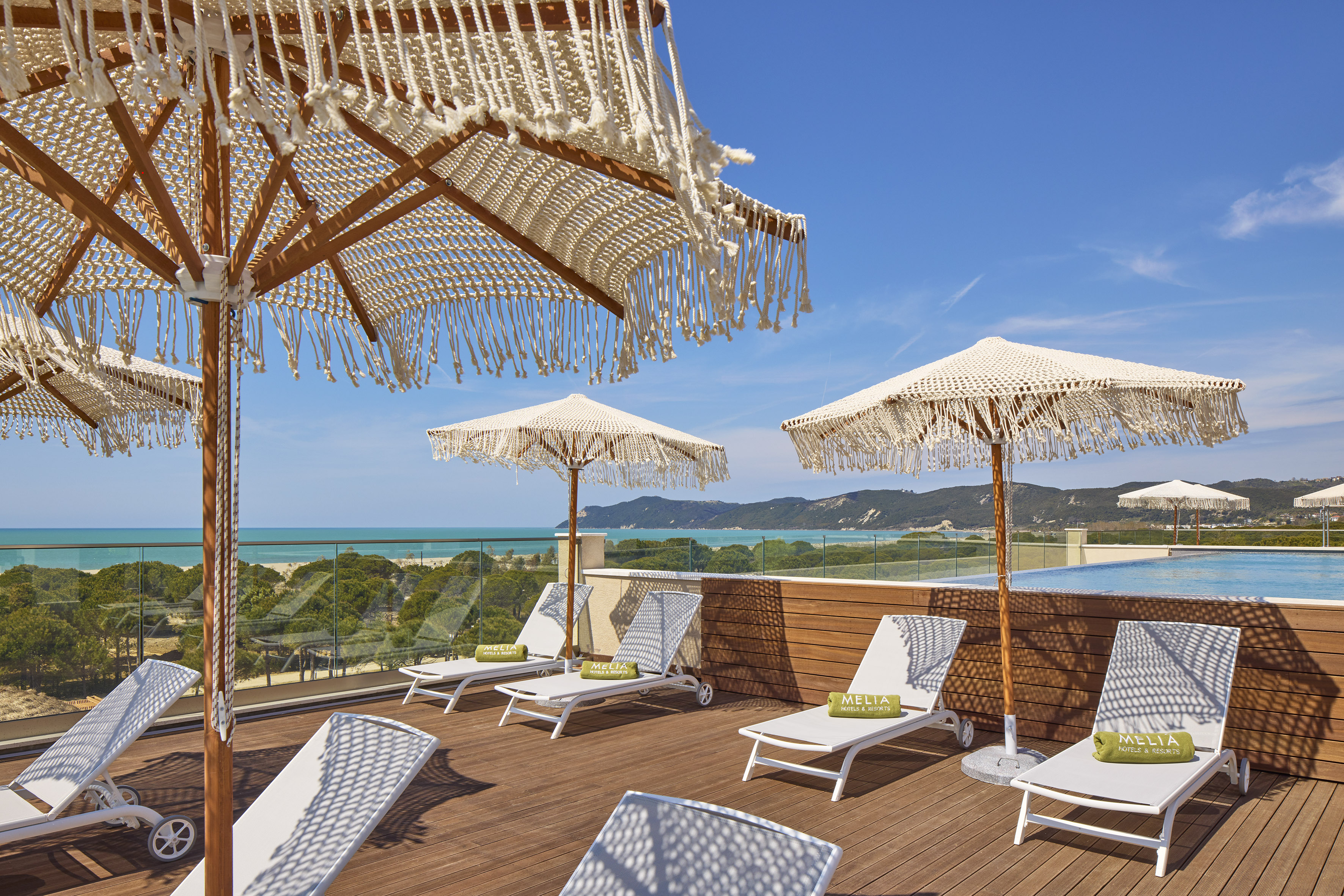 Resort rooftop terrace, ocean view, macrame umbrellas, sun loungers, and pool.