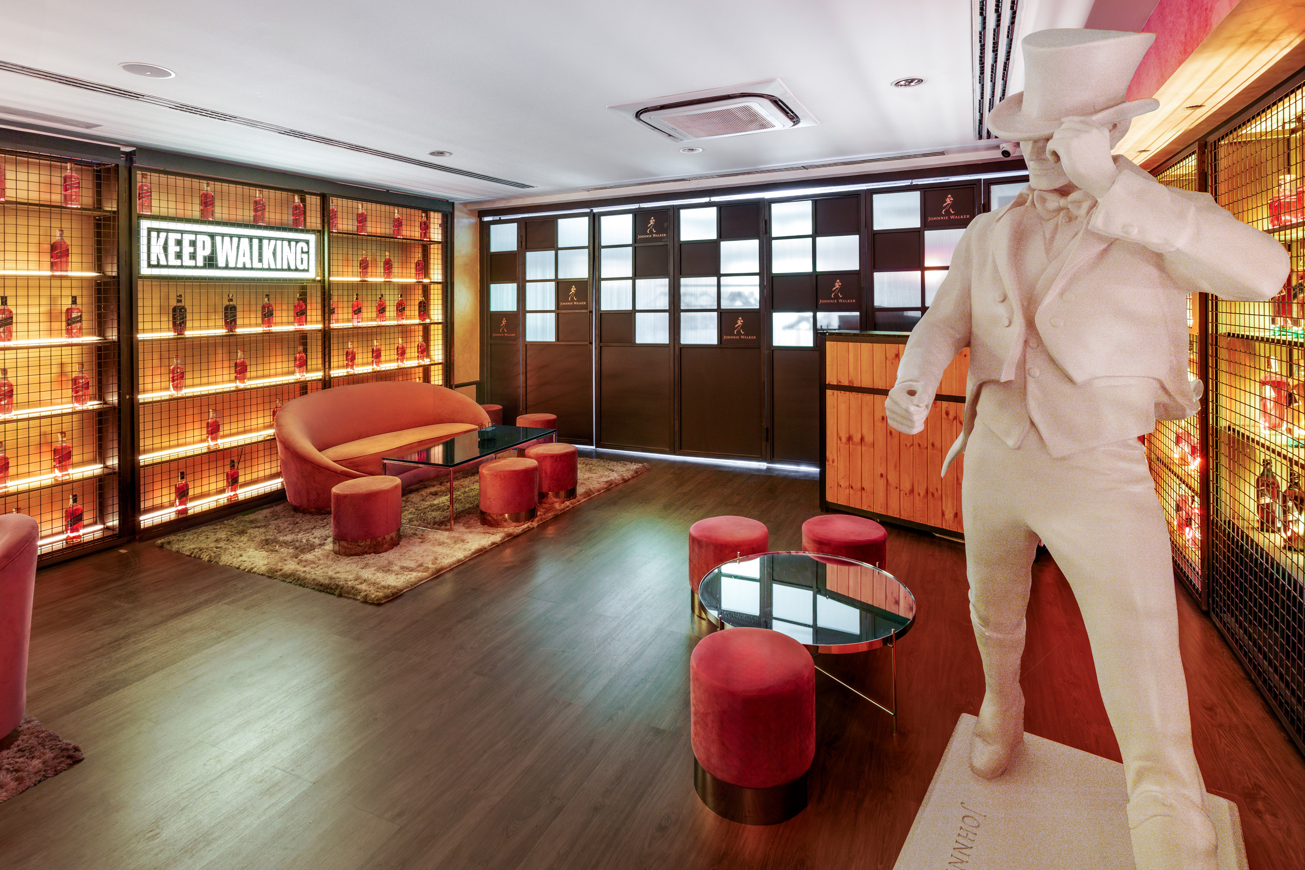 Johnnie Walker branded lounge: Striding Man statue, glowing whisky bottles, 'KEEP WALKING' sign.