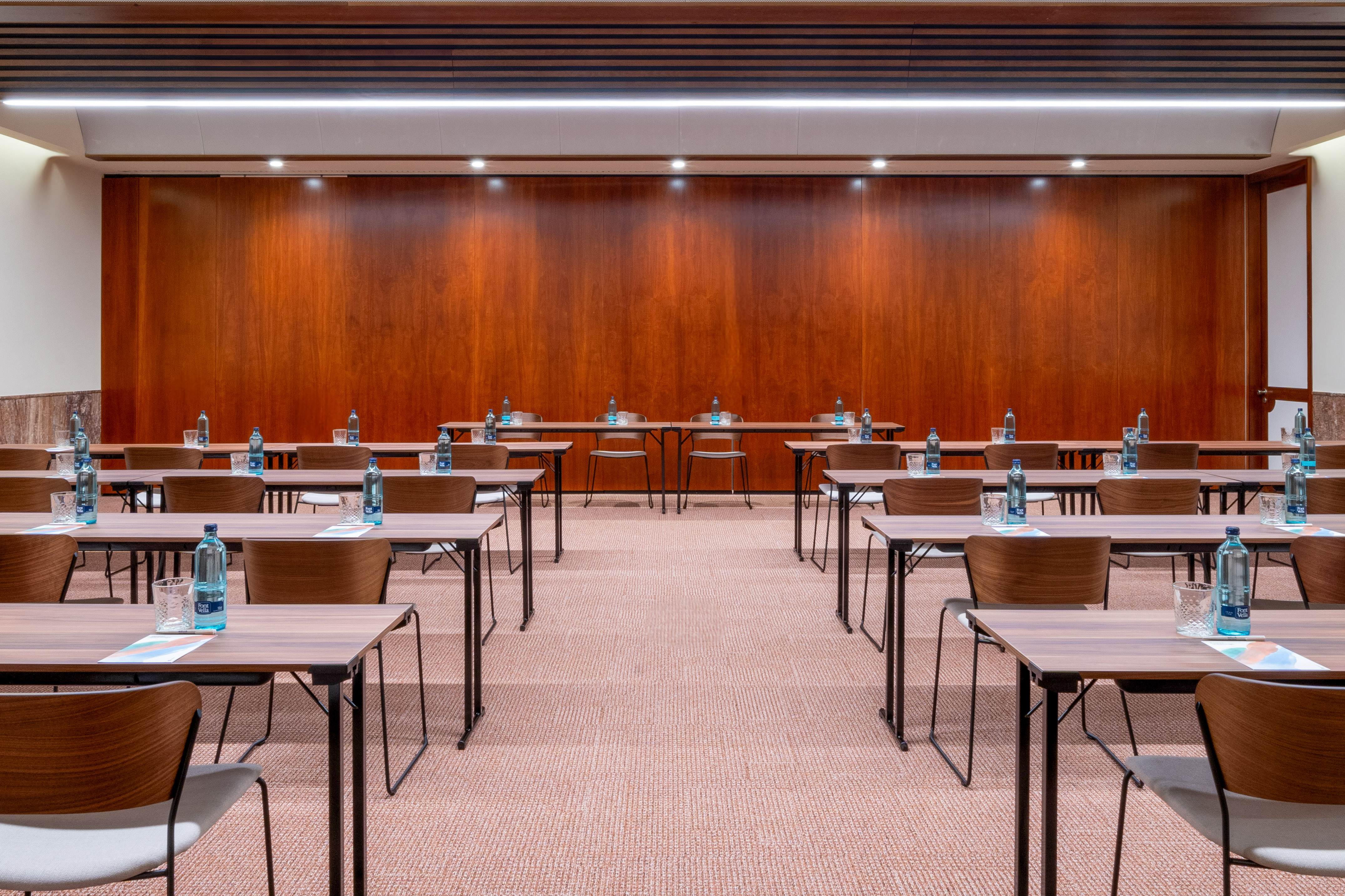 Empty modern conference room with tables, chairs, water bottles, wooden walls.