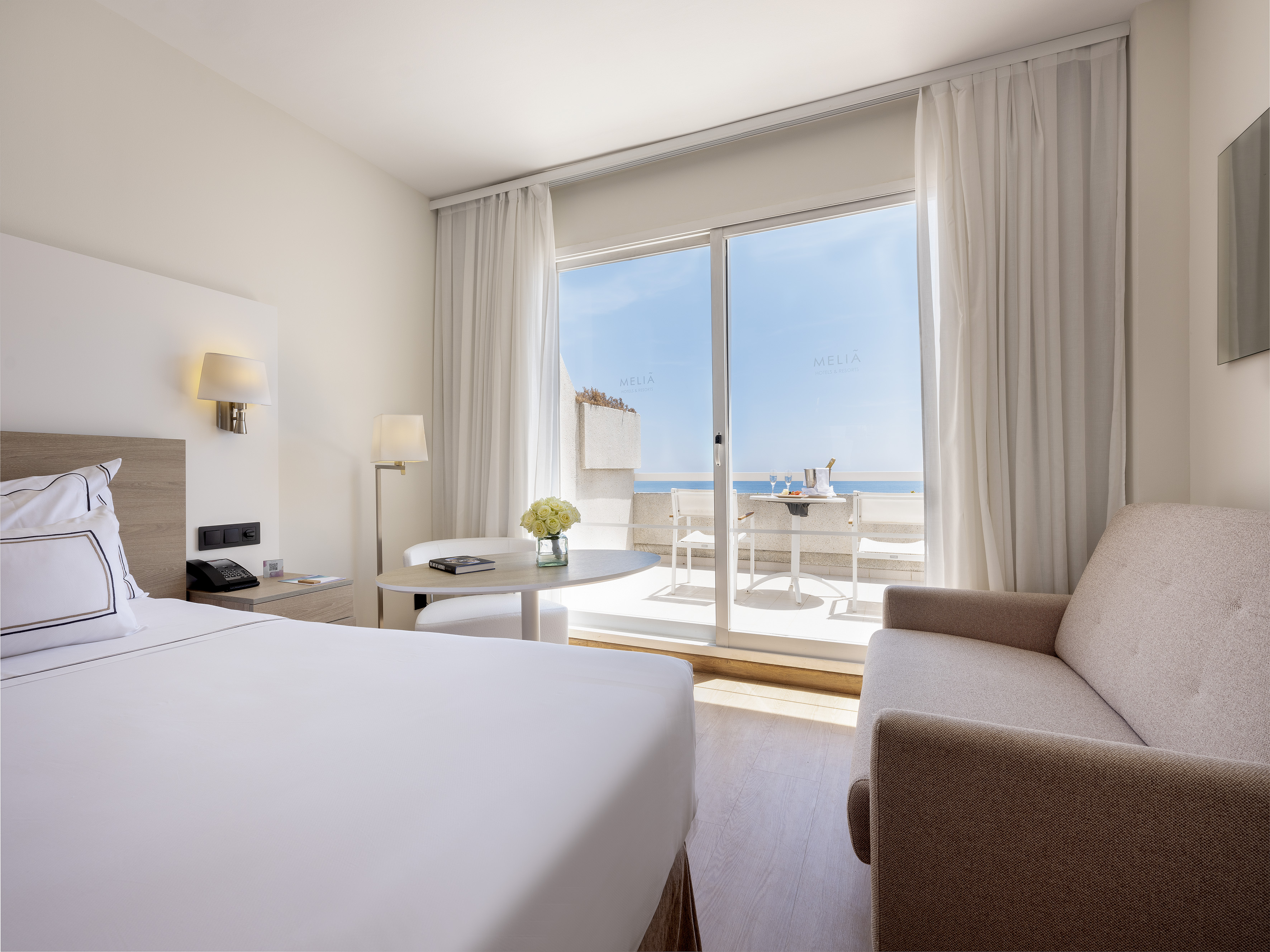 Meliá hotel room: sea view balcony, white bed, sofa, outdoor dining.