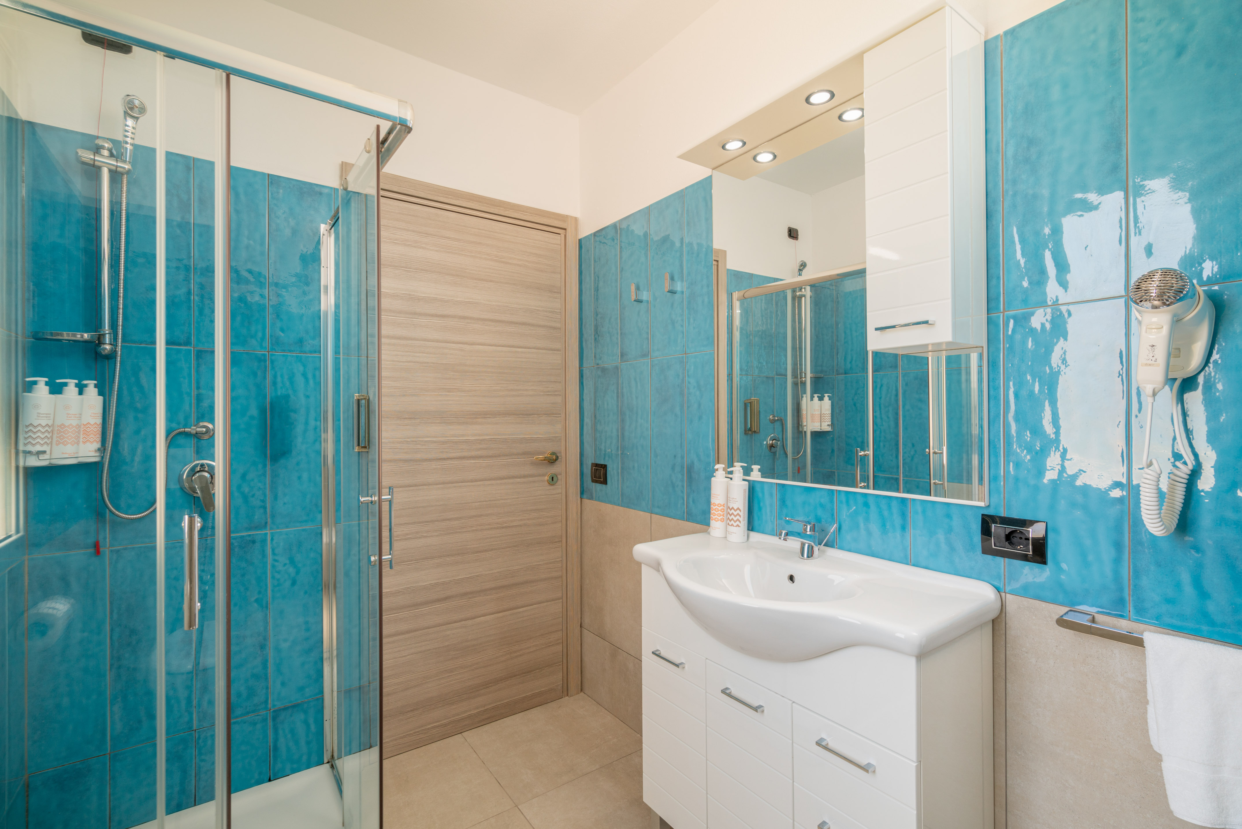 Modern bathroom with blue tiled walls, glass shower, white vanity, and mirror.