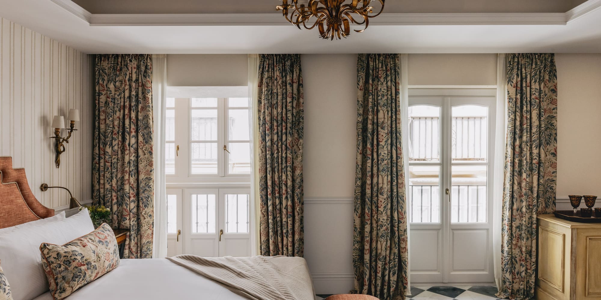 Dormitorio de hotel clásico con cortinas florales, cama y suelo ajedrezado.