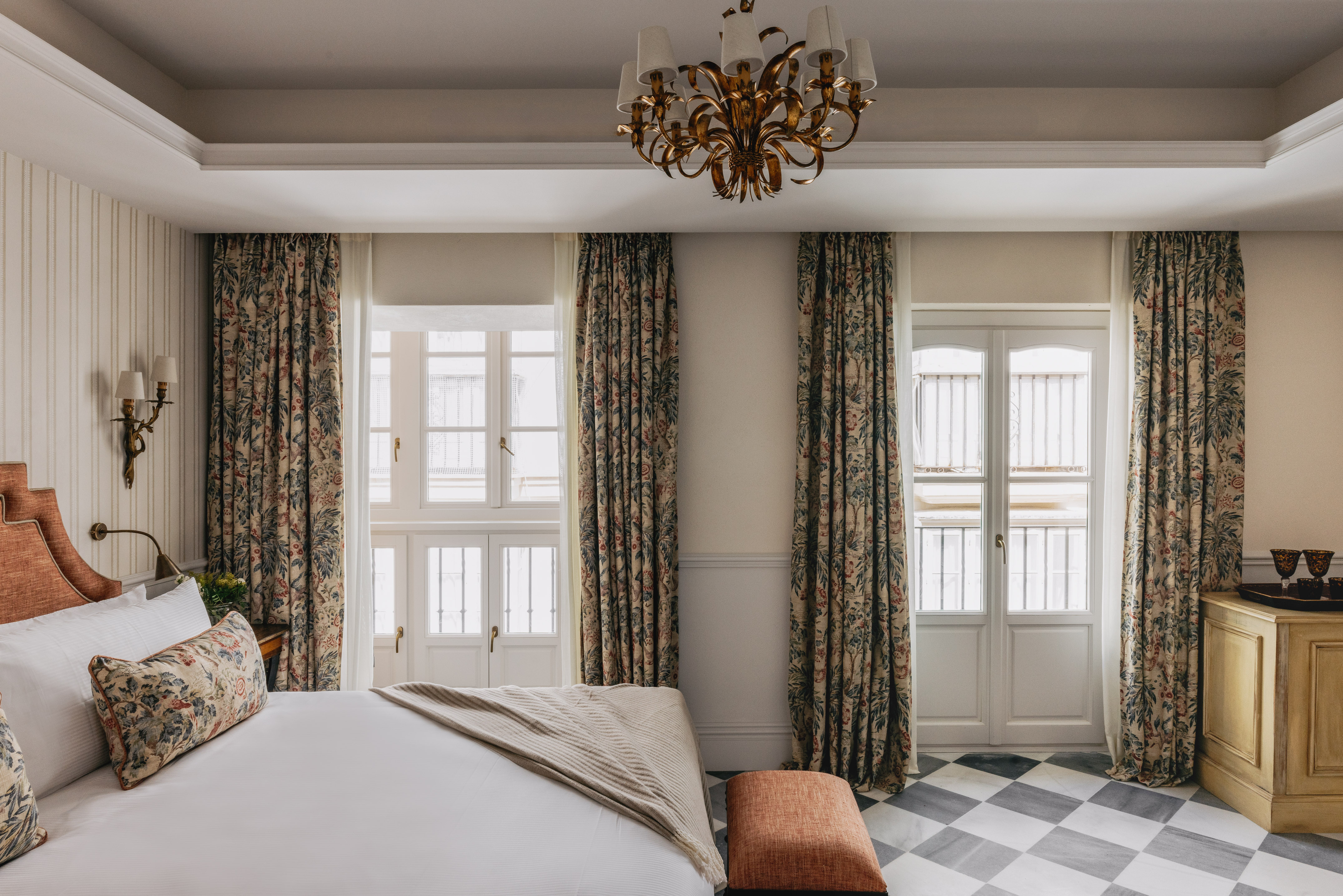 Dormitorio de hotel clásico con cortinas florales, cama y suelo ajedrezado.