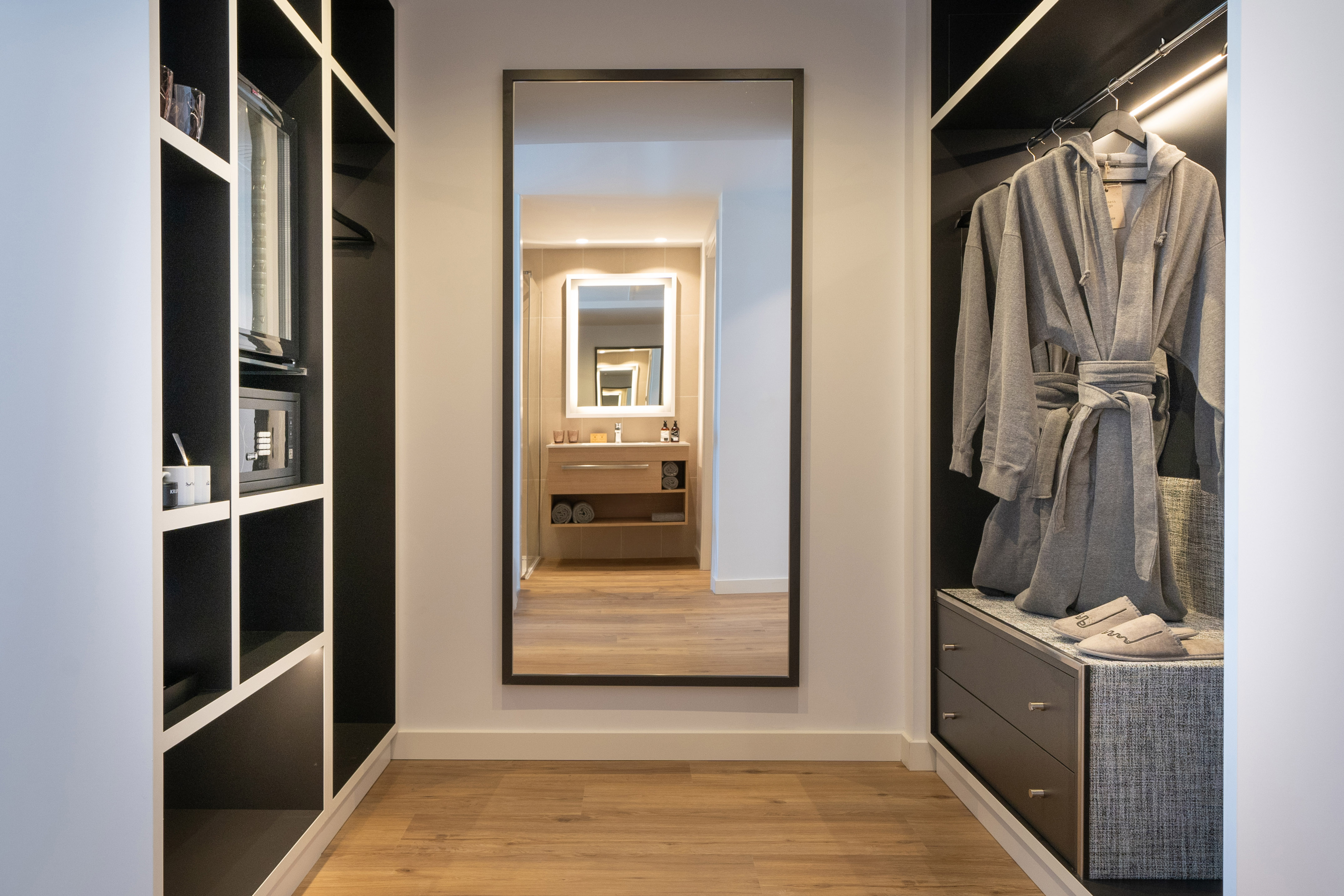 Modern hotel closet with bathrobes, mini-bar, safe, and full-length mirror.