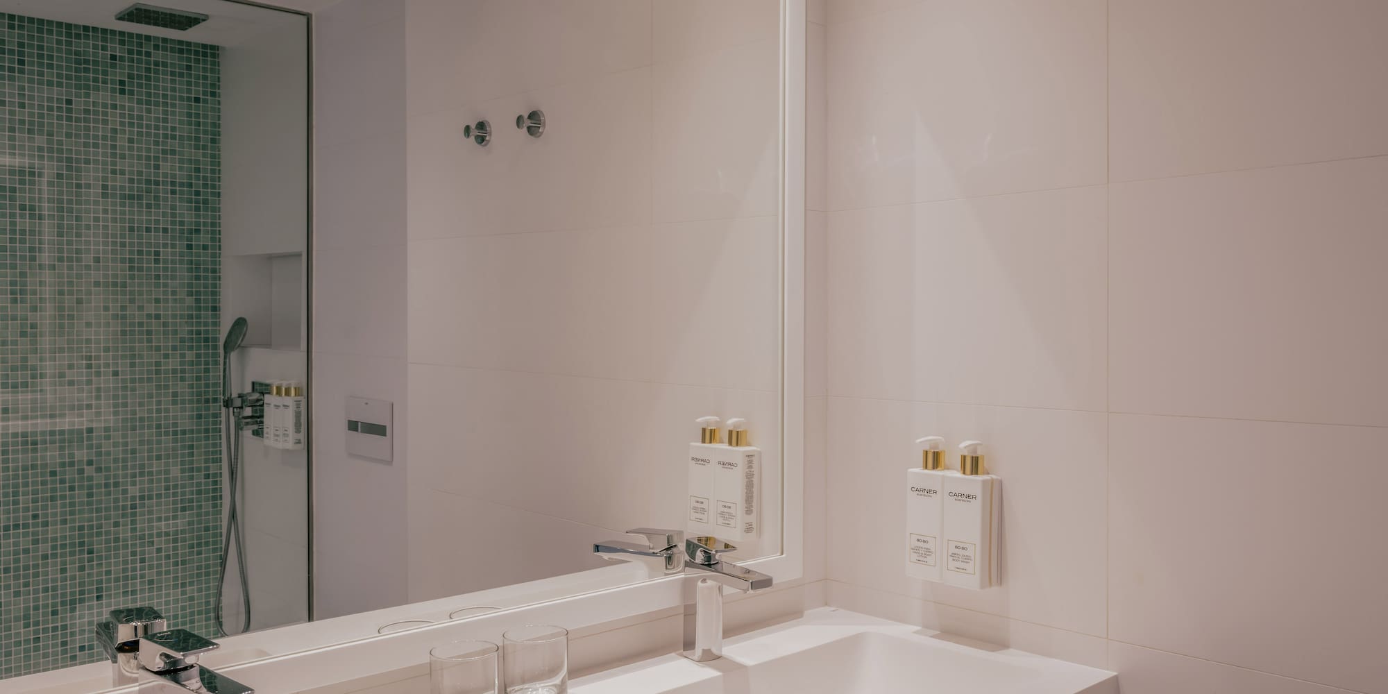 Modern bathroom with double sink vanity, chrome faucets, and green mosaic shower.