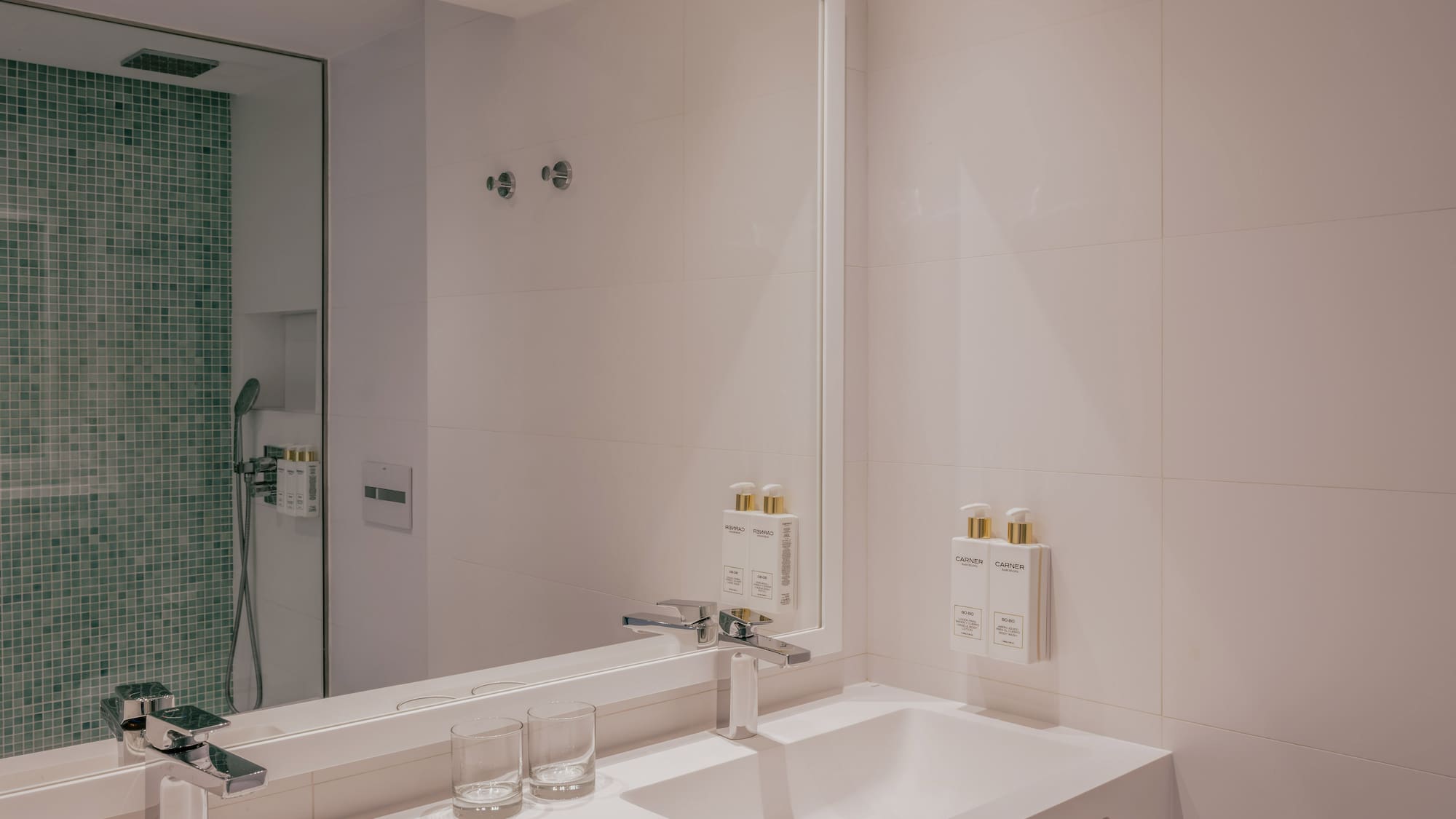 Modern bathroom with double sink vanity, chrome faucets, and green mosaic shower.