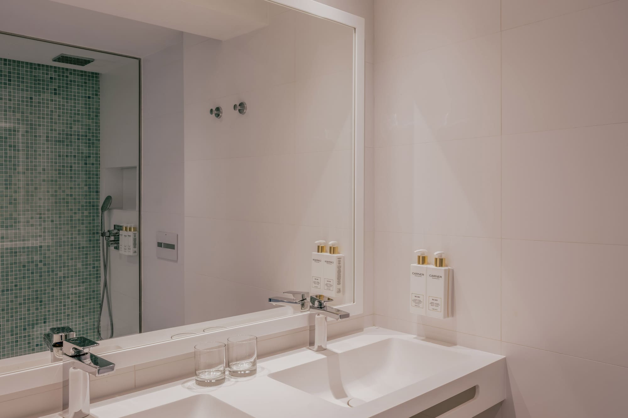 Modern bathroom with double sink vanity, chrome faucets, and green mosaic shower.