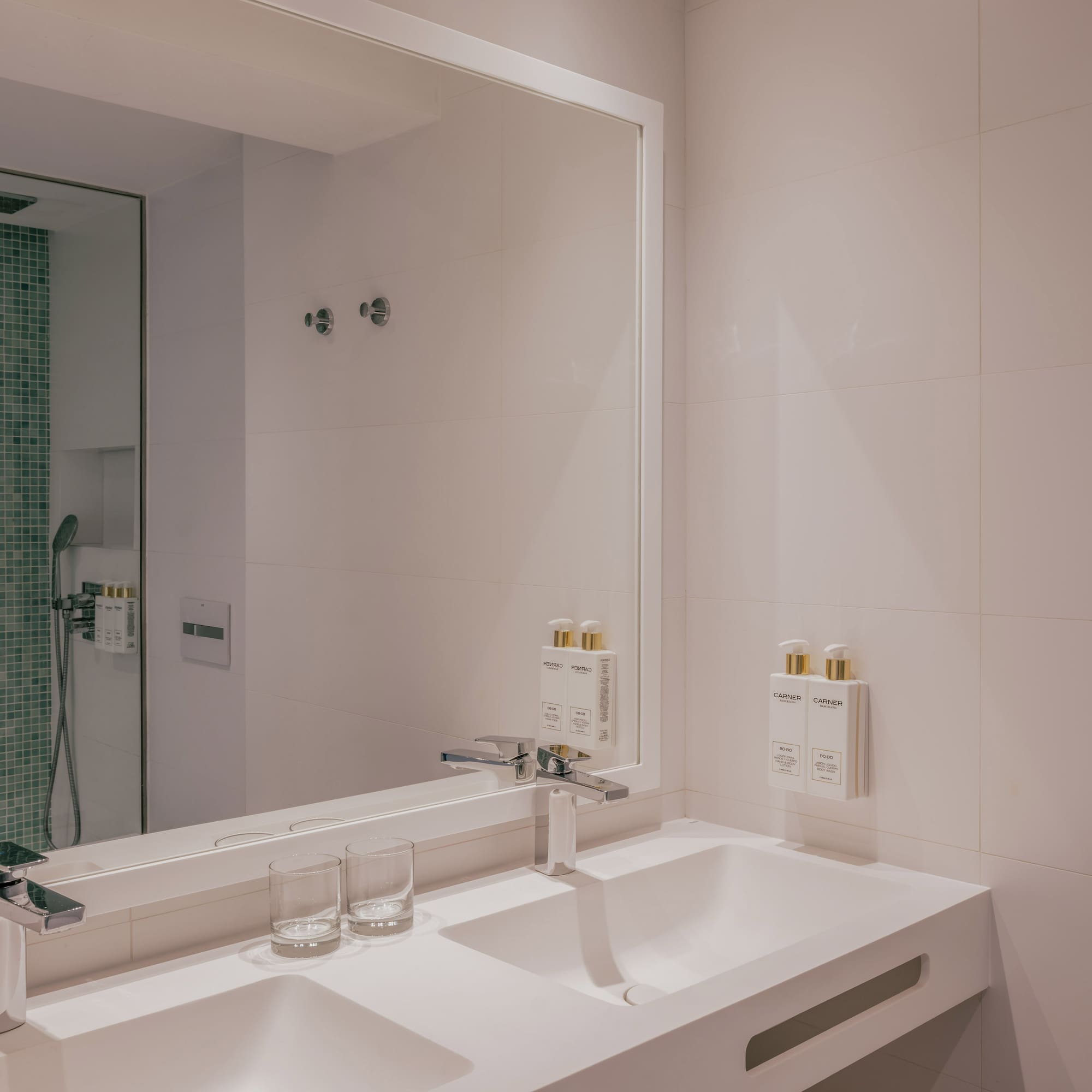 Modern bathroom with double sink vanity, chrome faucets, and green mosaic shower.