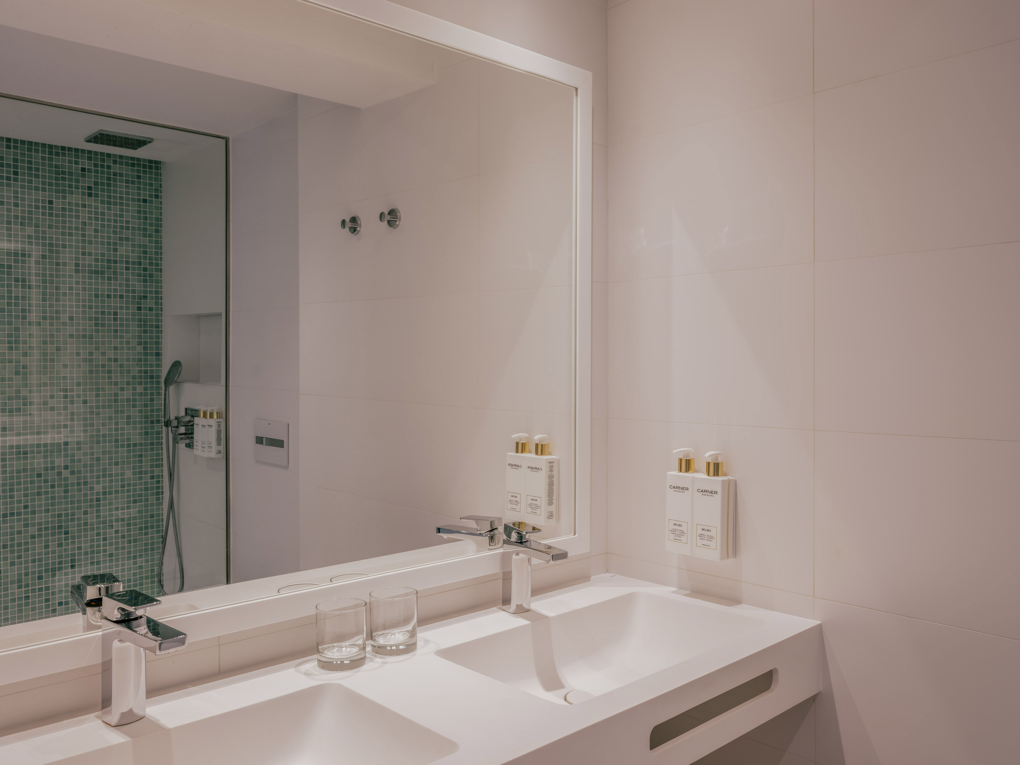 Modern bathroom with double sink vanity, chrome faucets, and green mosaic shower.