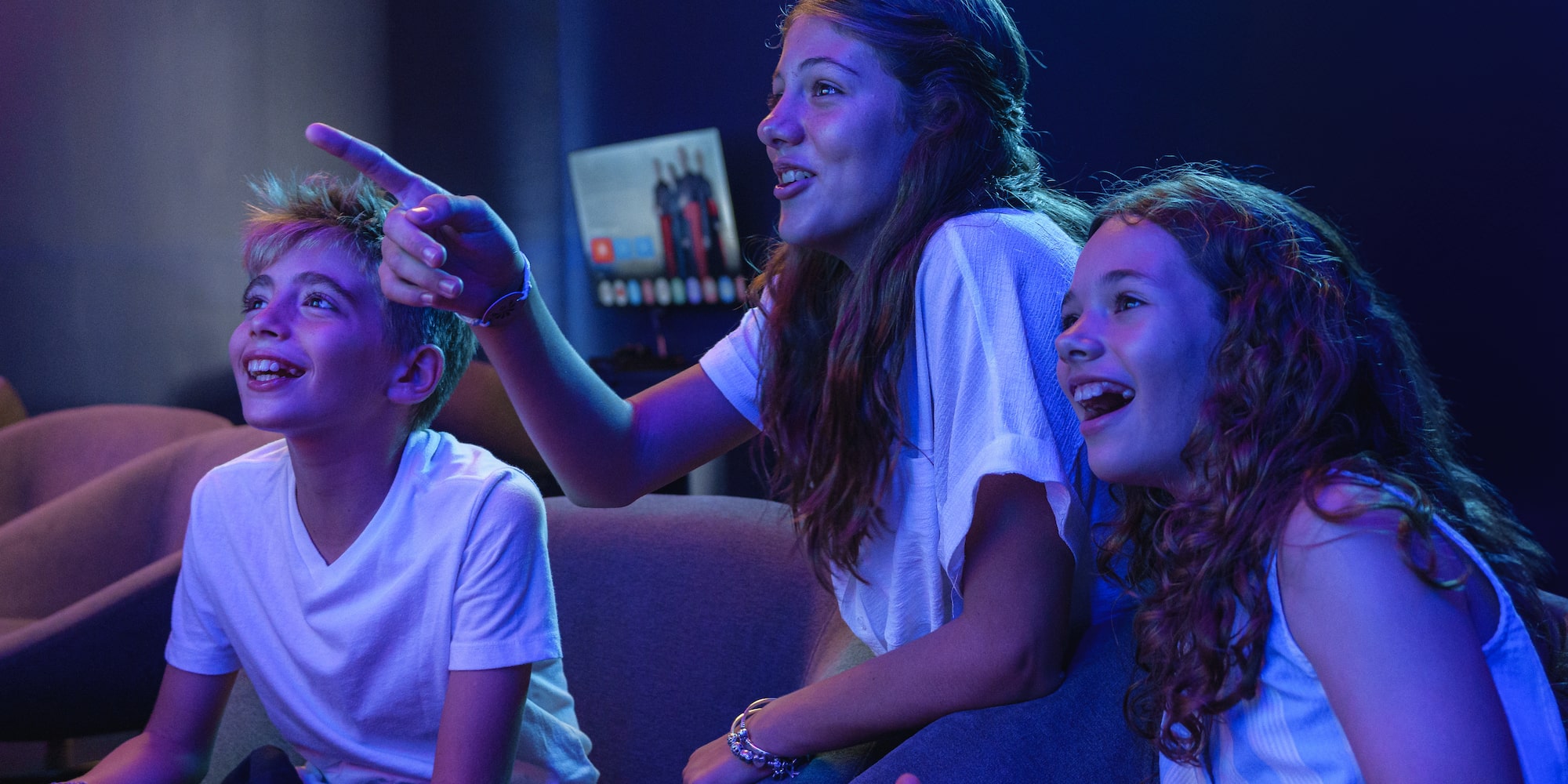 Excited teens and boy gaming with controllers, one pointing enthusiastically.