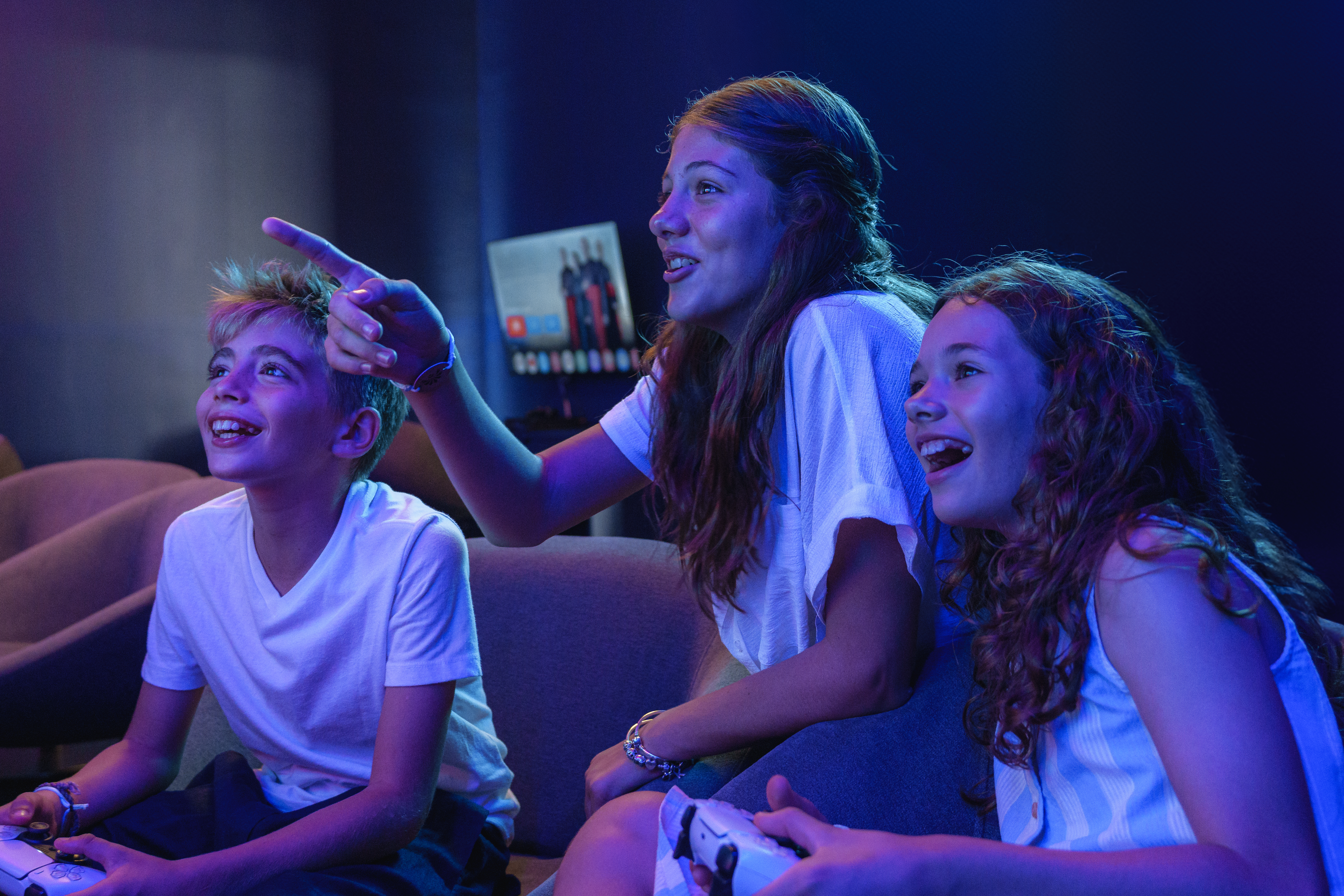 Excited teens and boy gaming with controllers, one pointing enthusiastically.