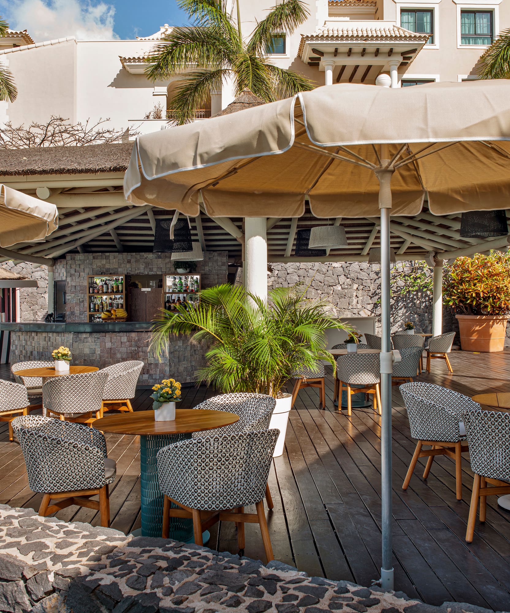 Outdoor resort bar patio with wooden deck, umbrellas, and palm trees.