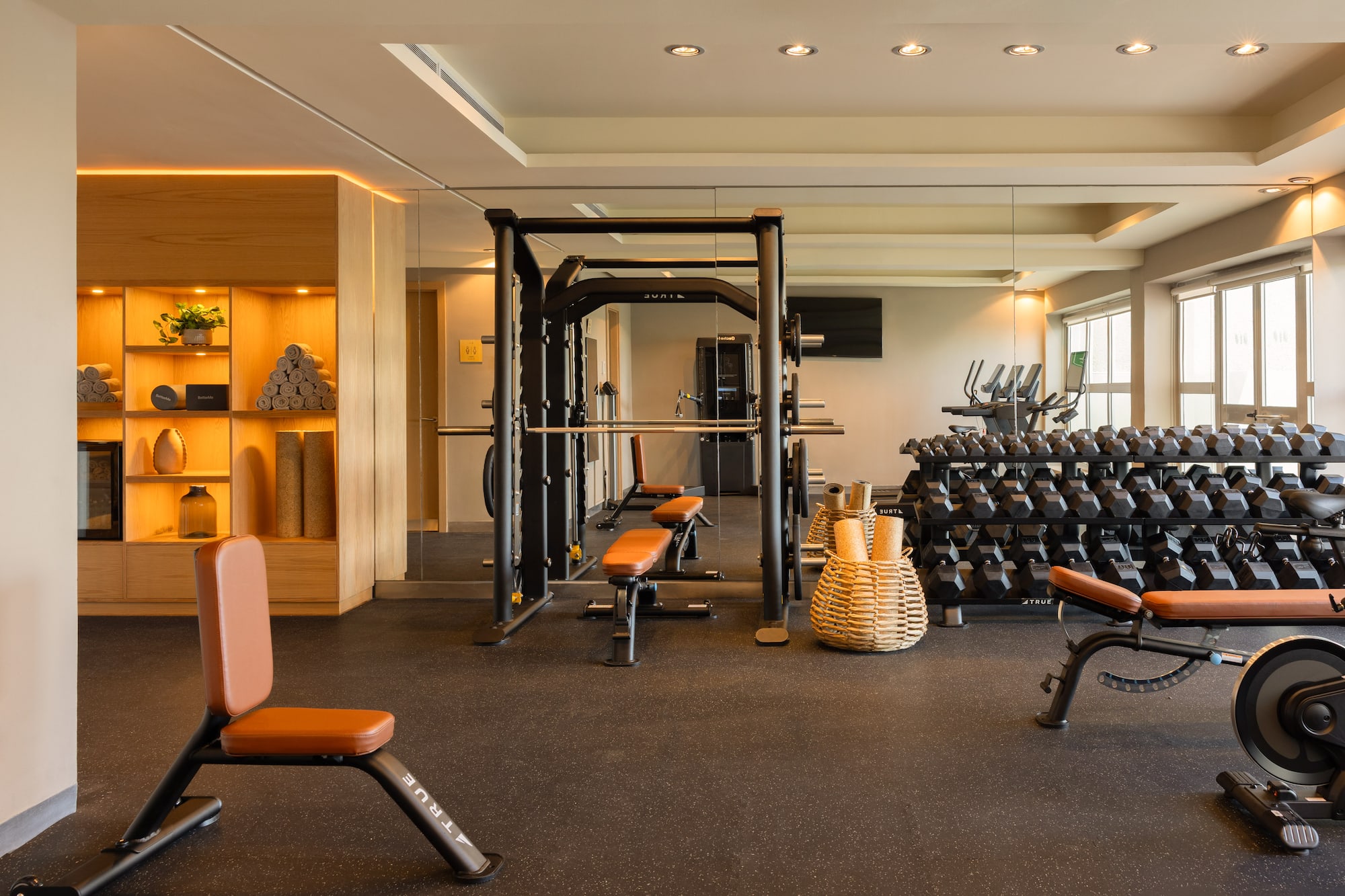 Well-lit modern gym with dumbbells, squat rack, and fitness benches.