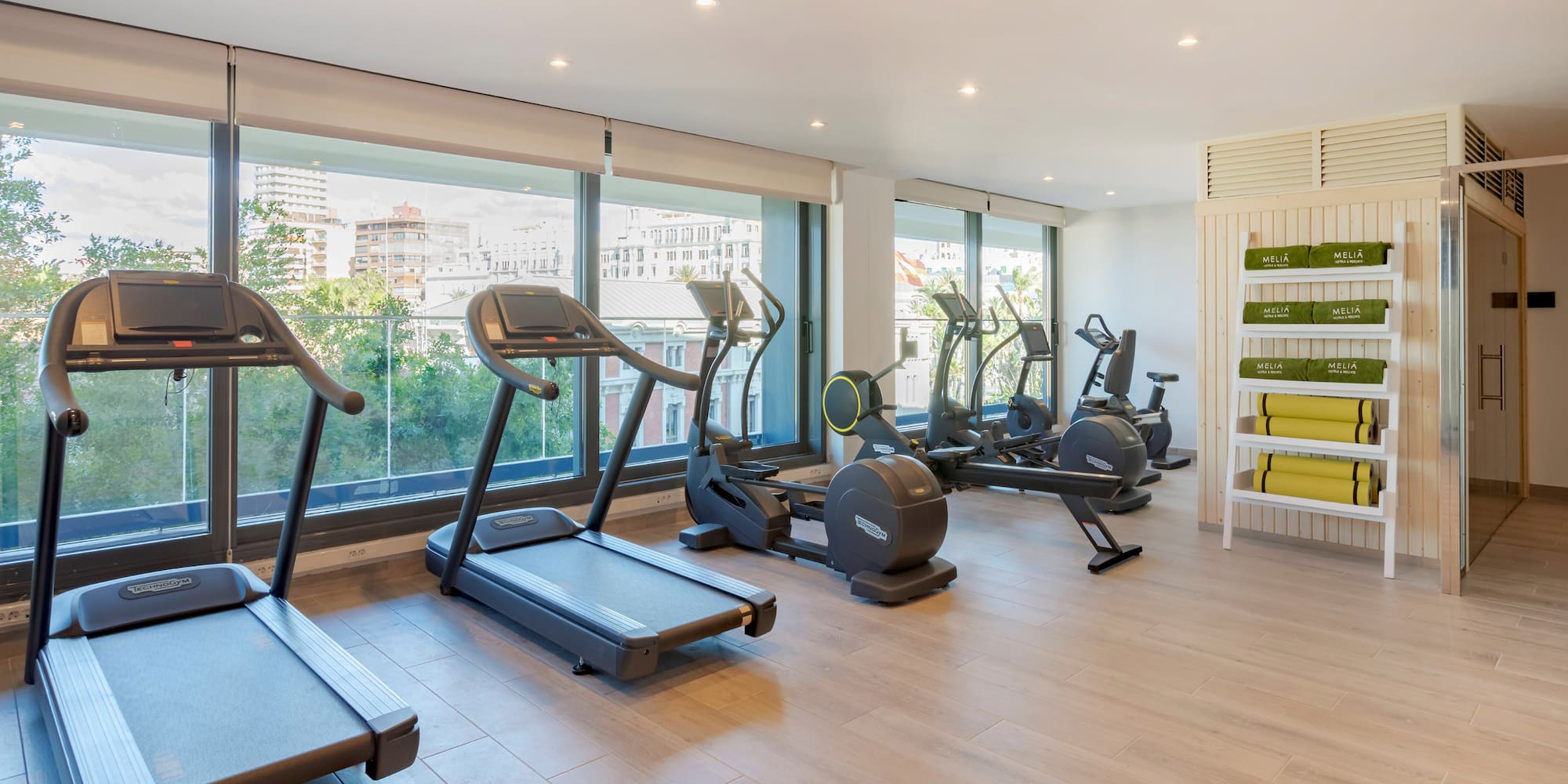 Moderno gimnasio Meliá con máquinas de ejercicio y vista a la ciudad.